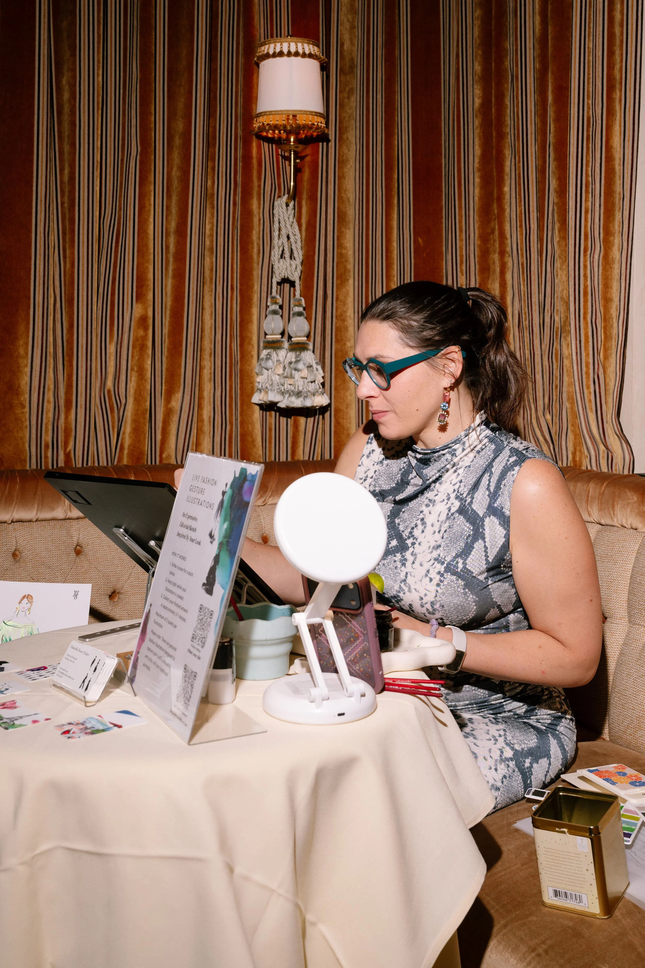 Danielle Rose Fisher sketching a live fashion illustration on a digital tablet at the Angel Ball Launch Party