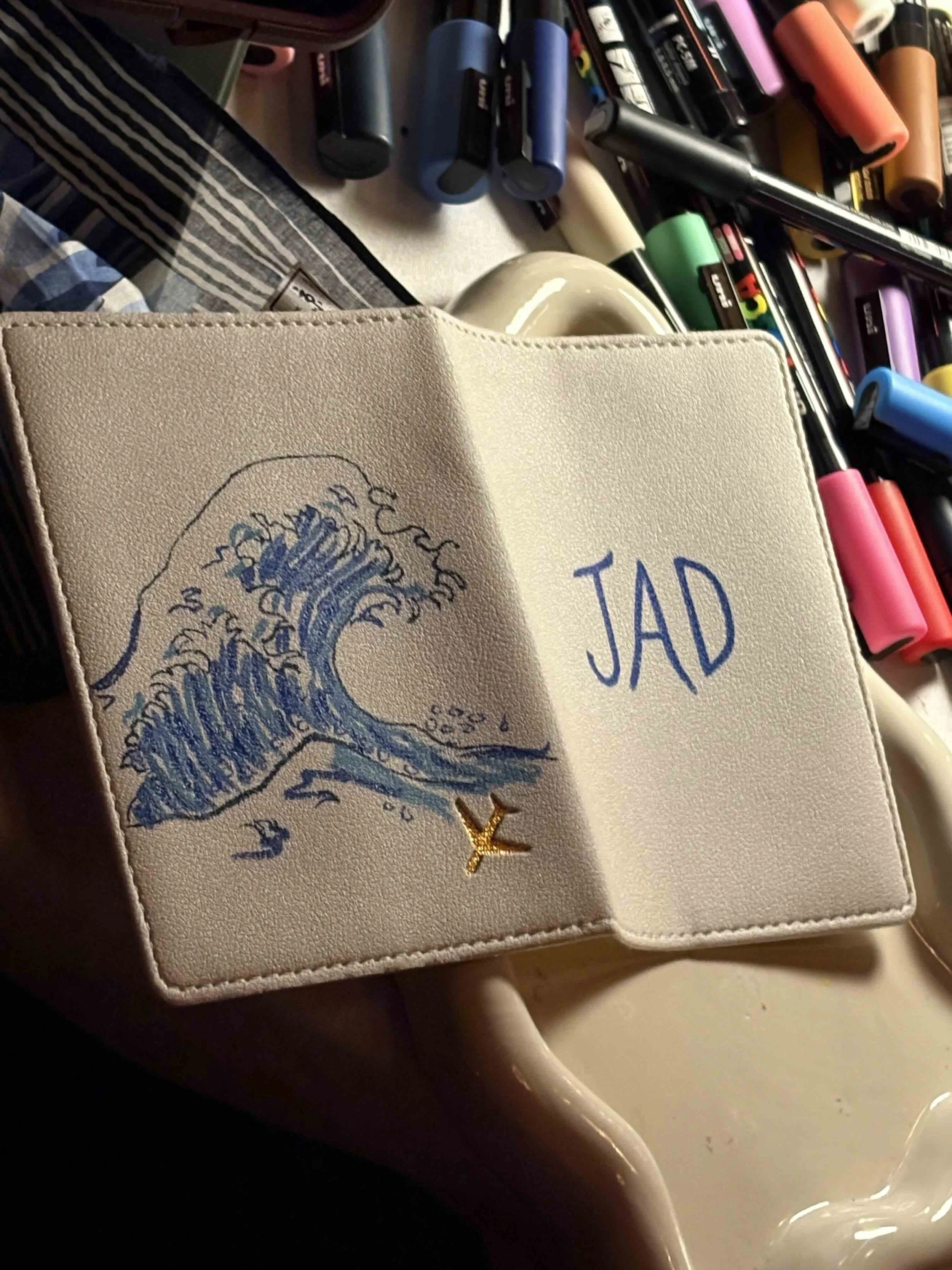 Guest at The Young Angels Gala holding a blue glitter passport holder hand-painted with a wave design and monogram — live illustration by Danielle Rose Fisher NYC