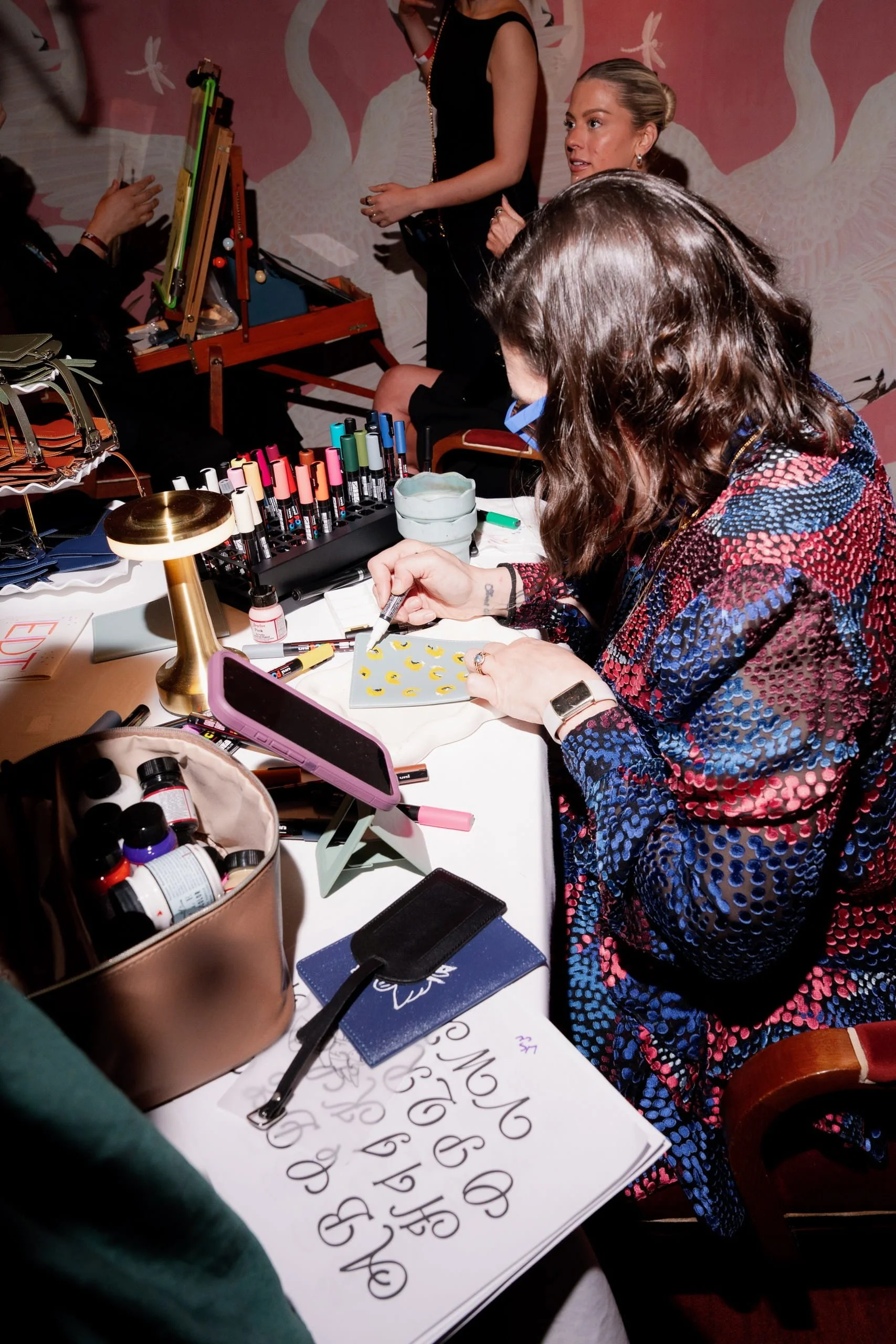 Close-up of Danielle Rose Fisher painting a custom crescent moon design on a passport holder live at The Young Angels Gala