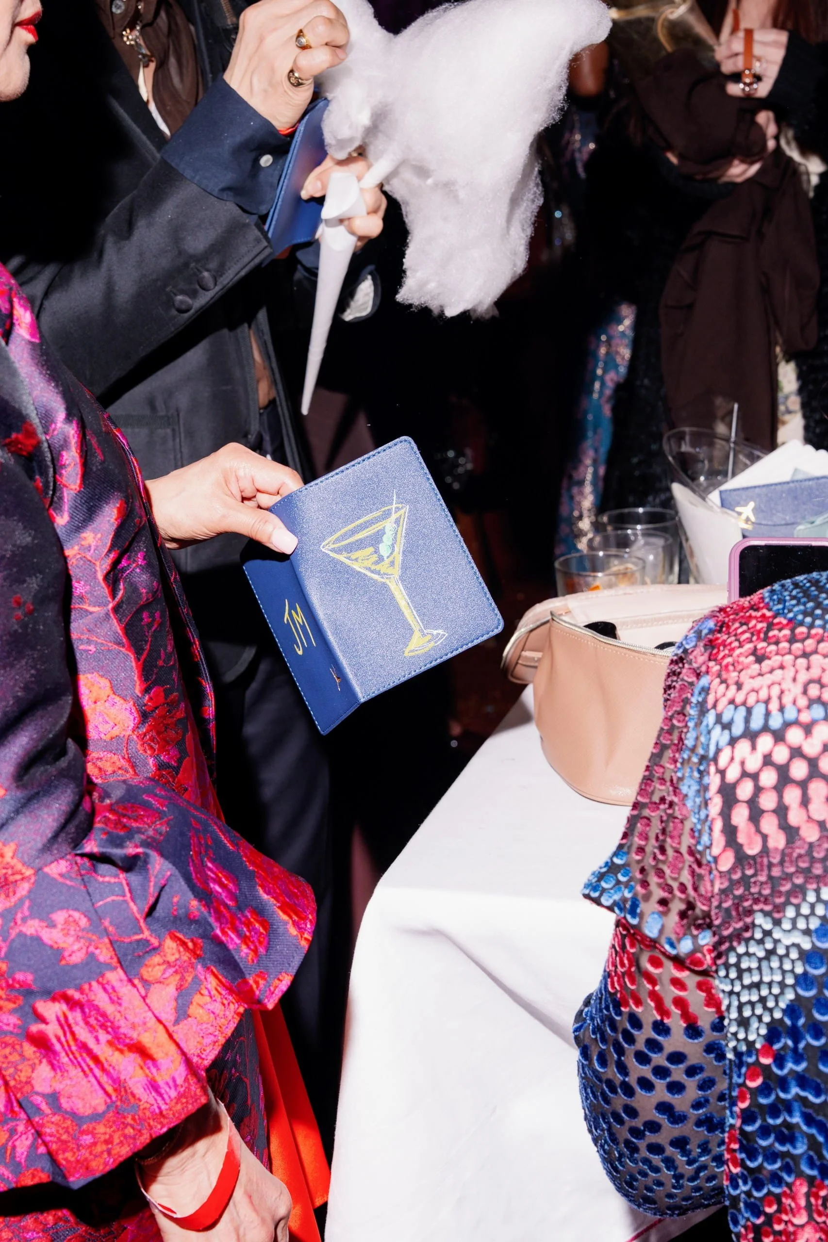 Guest at The Young Angels Gala holding a blue glitter passport holder hand-painted with a gold martini glass and monogram — live illustration by Danielle Rose Fisher NYC