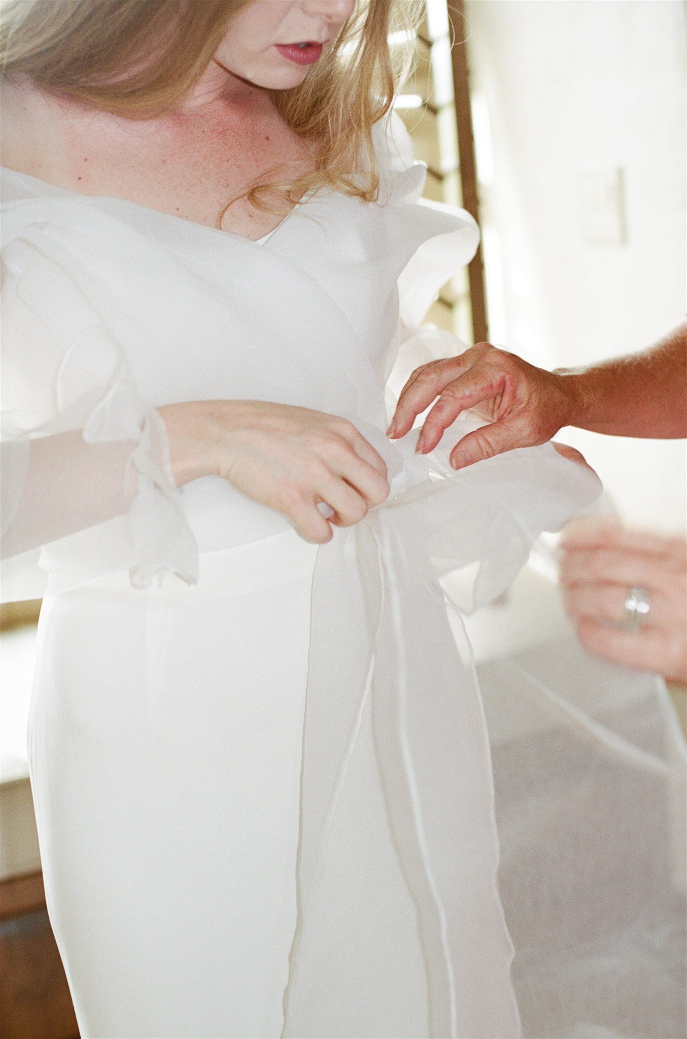  A bride getting ready for her wedding in The Label ROSE wedding dress, a fitted strapless gown with a sheer organza long sleeve wrap blouse 