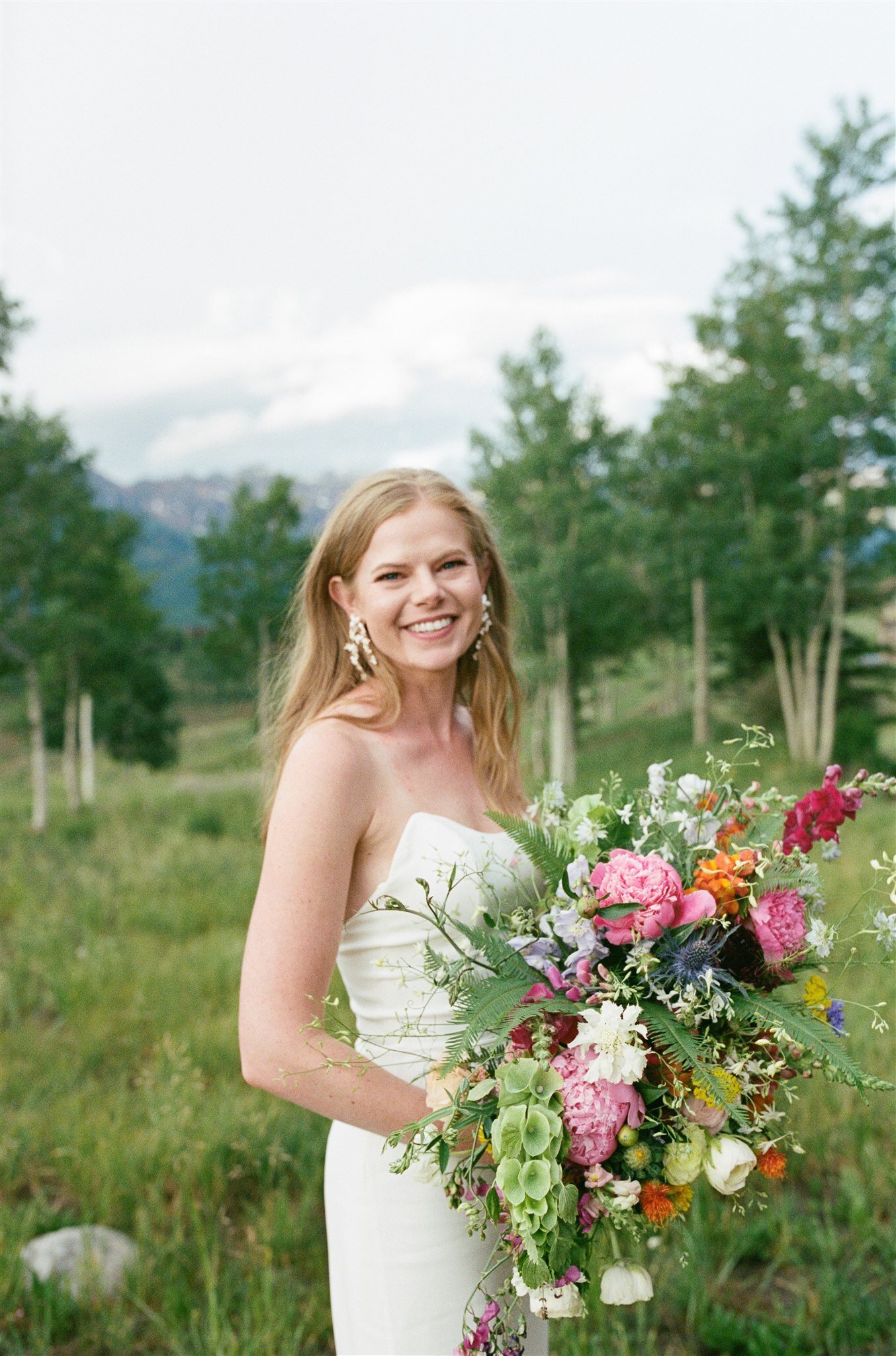  A bride in Telluride, Colorado smiling holding a large floral bridal bouquet and wearing ROSE by The Label 