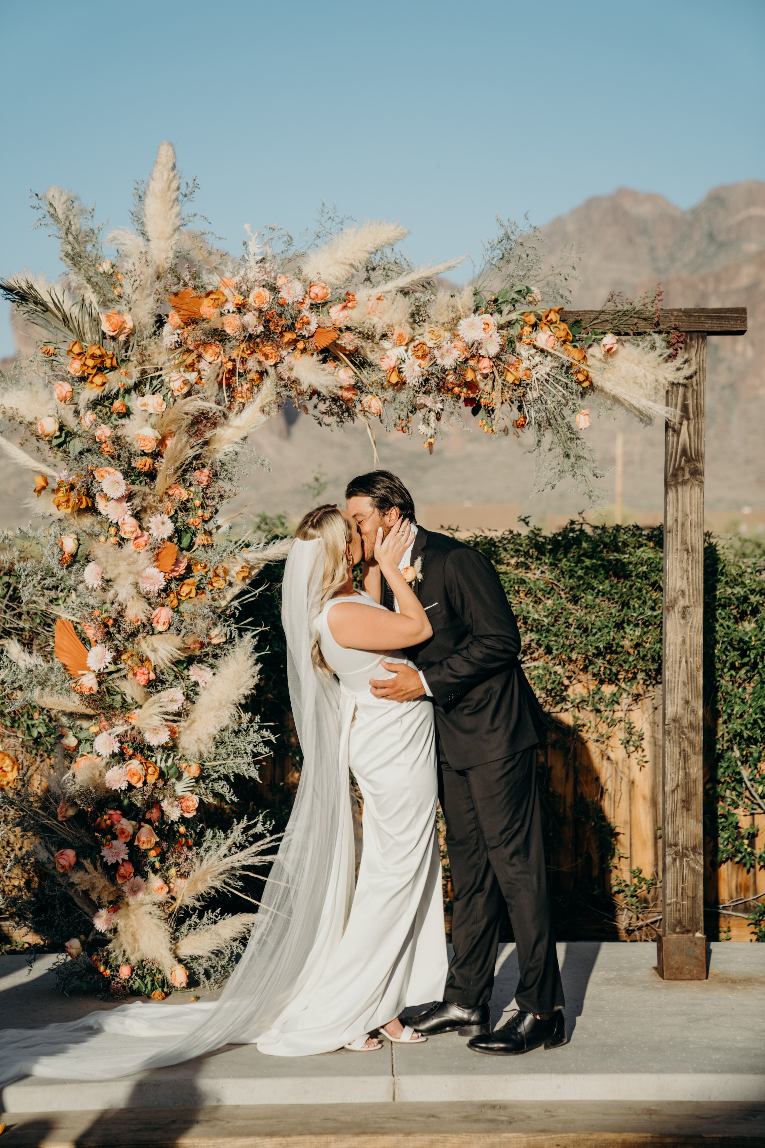 a pampas grass and orange boho floral installation on arch for ceremony.