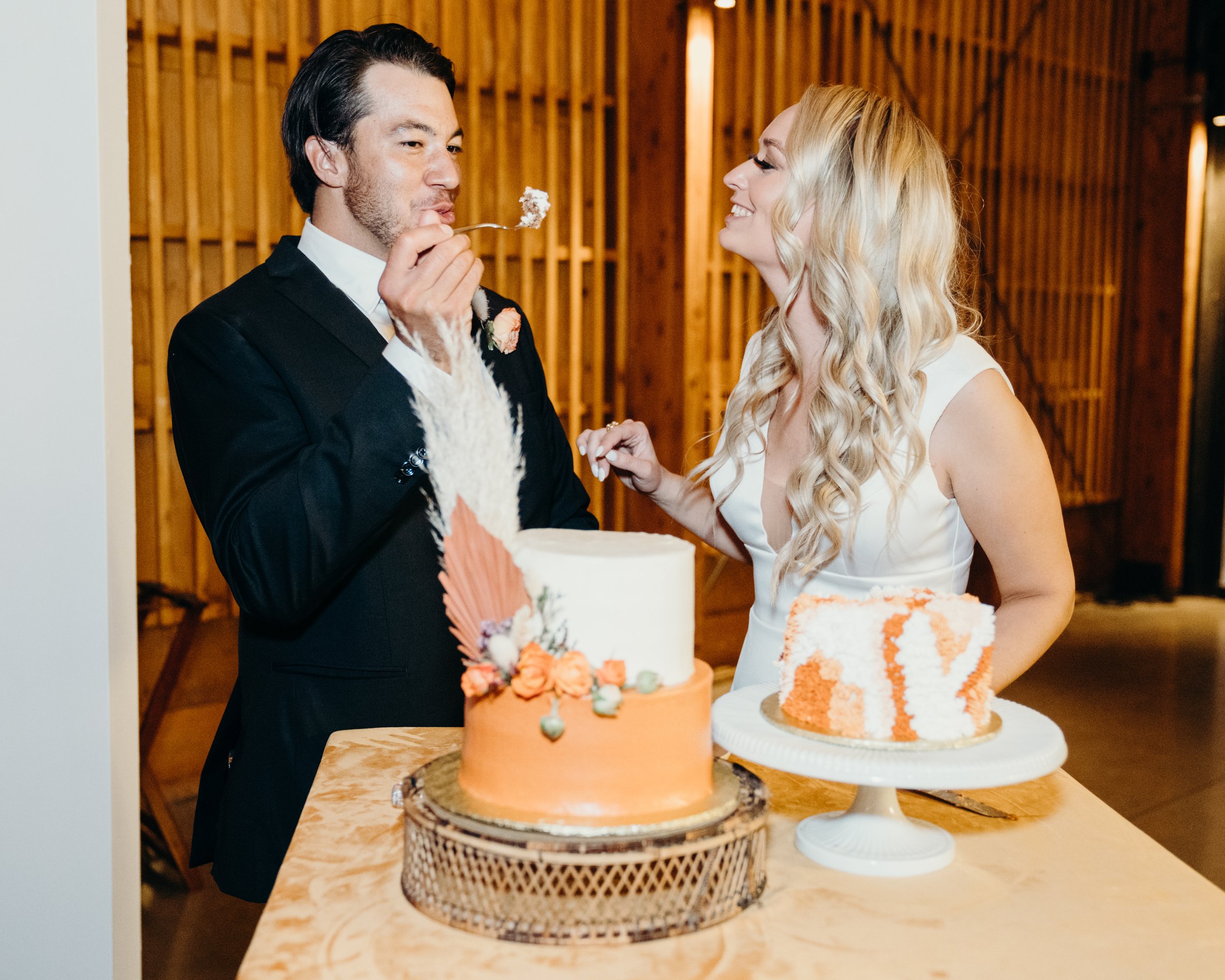 the bride and groom sharing thier piece of cake from the trio of cakes including a retro shag carpet frosting cake in orange hues.