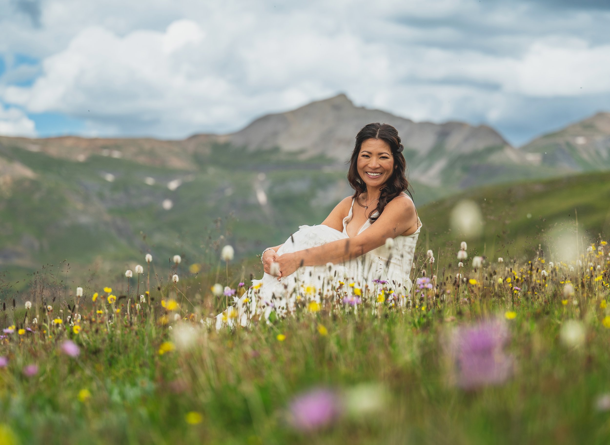 a bridal portrait in a wildflower field atop a mountain in colorado featuring a floral applique wedding dress from annabe bridal boutique