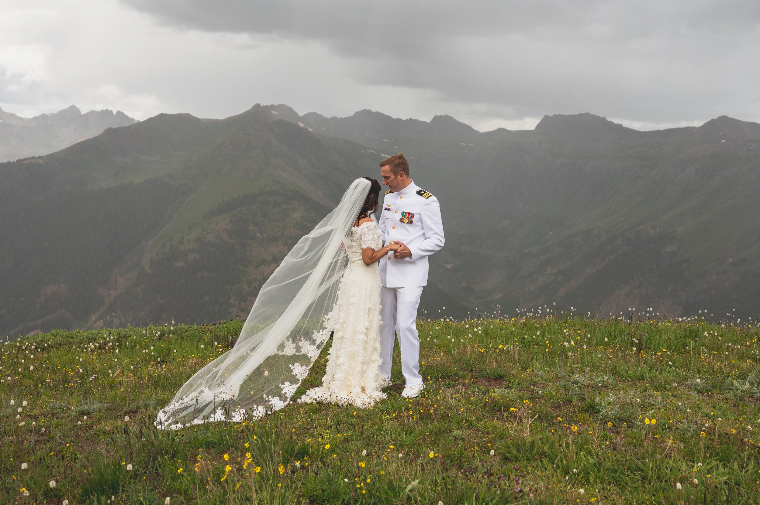 a military wedding on a colorado mountain with the bride wearing a floral wedding gown and veil in a wildflower field