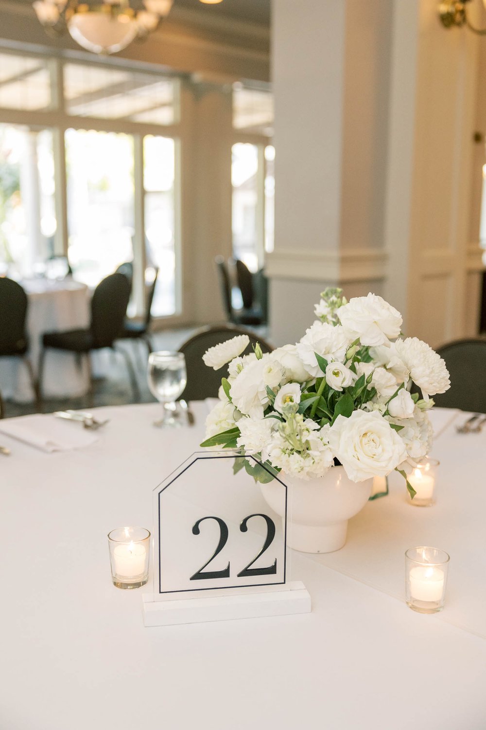  a chic wedding reception tablescape with white florals and linens, and a geometric acrylic table number 