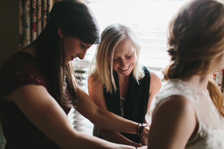 mother and friend helping the bride put on her dress