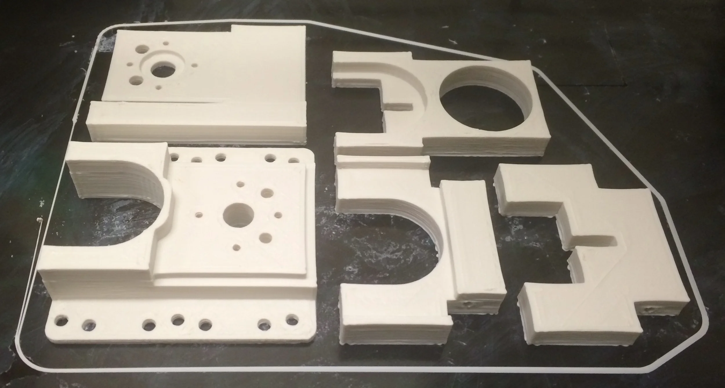 CUSTOM PARTS ON THE BED OF 3D PRINTER. THE MID MOUNT AND PLUNGER UNIT WERE BROKEN INTO SEPERATE PARTS FOR PRINTING AND REASSEMBLED LATER.