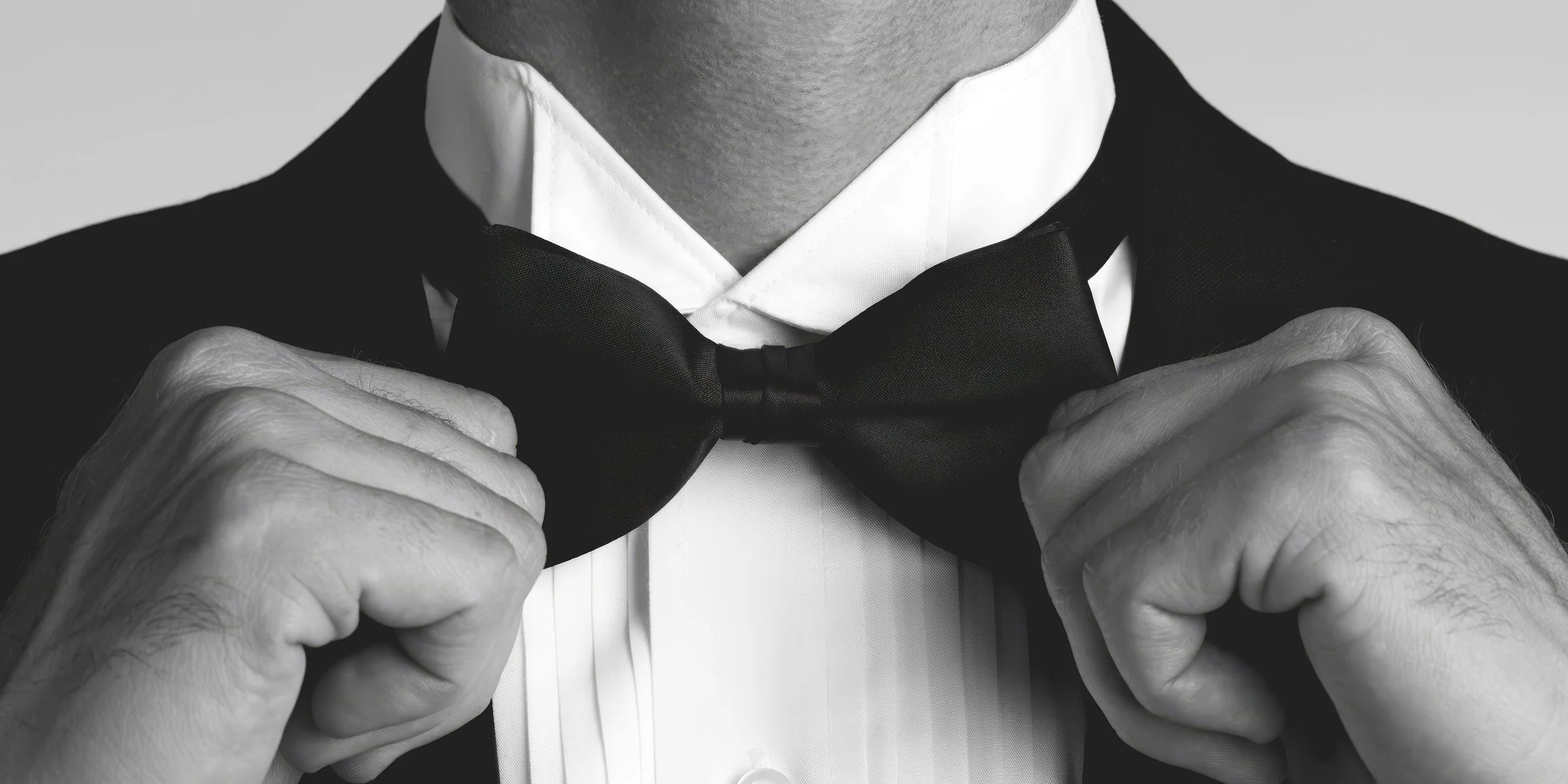 Black and white photograph of a man adjusting his bow tie