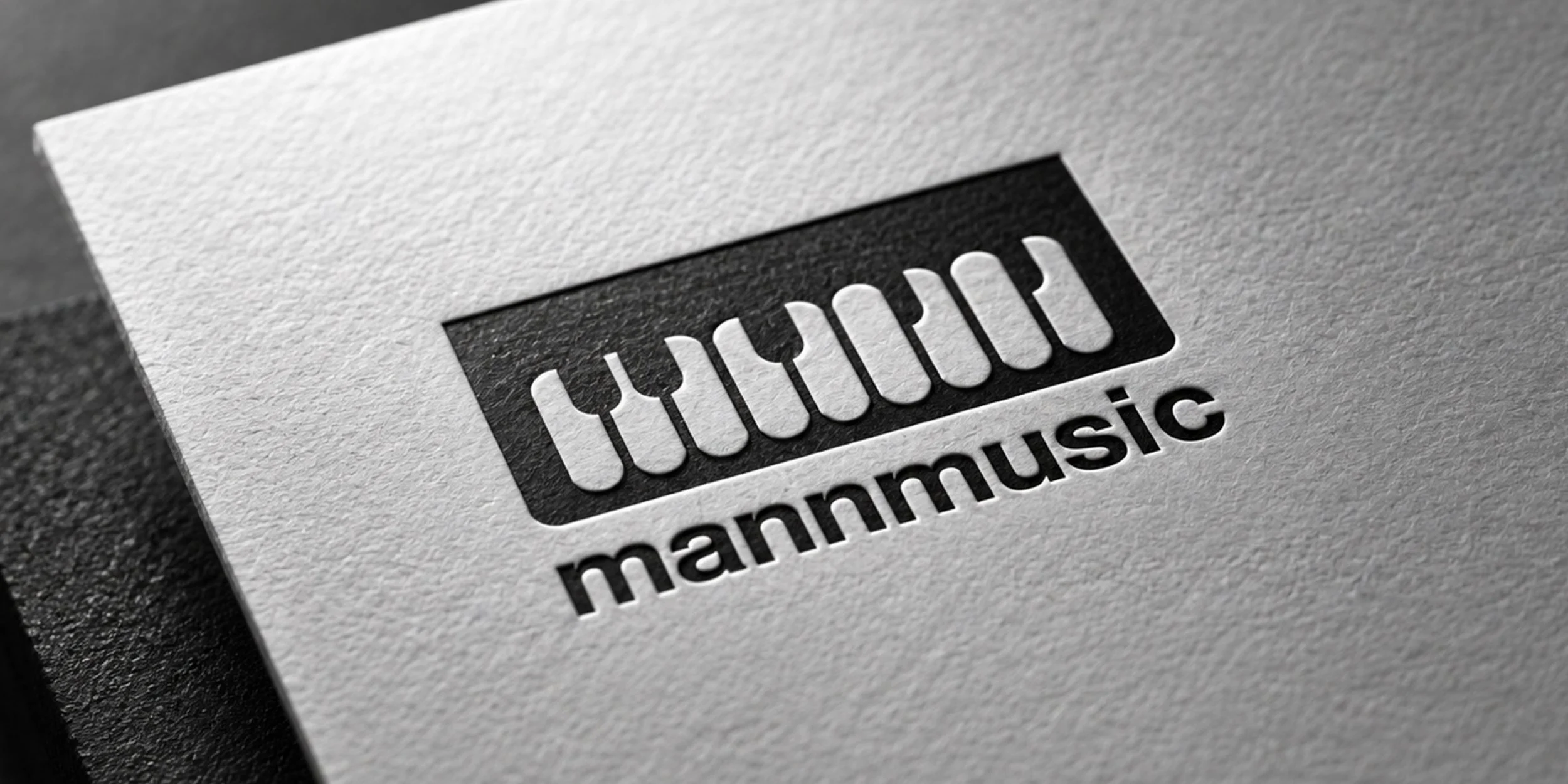 MannMusic logo embossed on textured white paper, showcasing the monochrome piano-inspired identity in a close-up mockup.