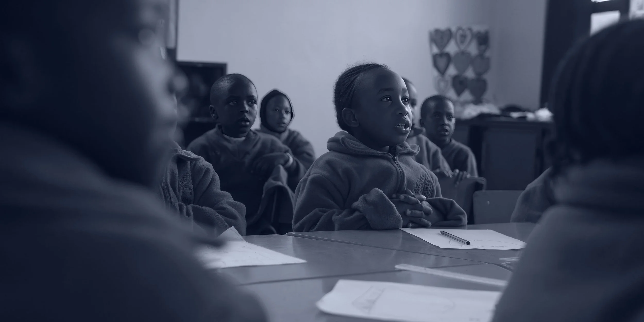 Schoolchildren sitting together in a classroom, presented in monochromatic navy tones as part of the Flying Kites brand identity showcase.