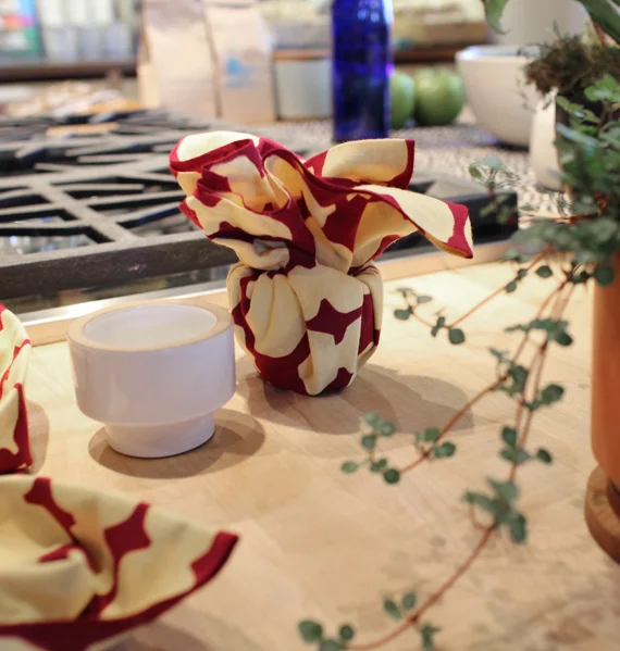 Magumi took inspiration from the shape of the candle holder by tucking the fabric into it's cavity and creating a flower with the ends. This is a great example of letting the object dictate how the fabric forms around it. Maybe this will work for wrapping a small cup too!