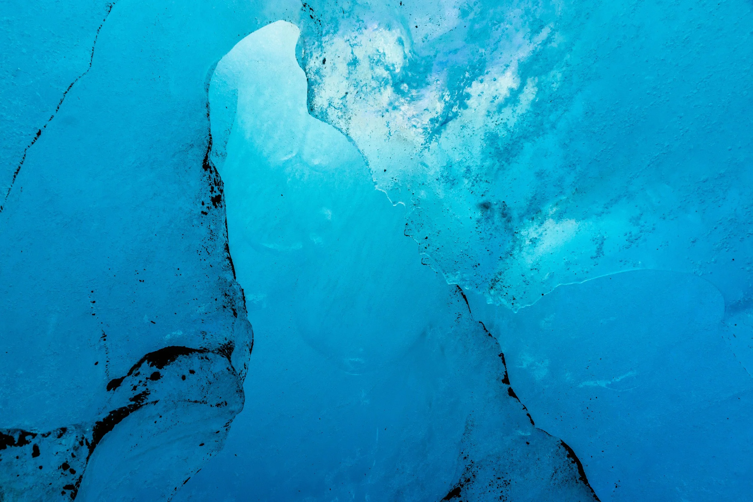 Close-up of ice or glacier with shades of blue and black cracks and textures.