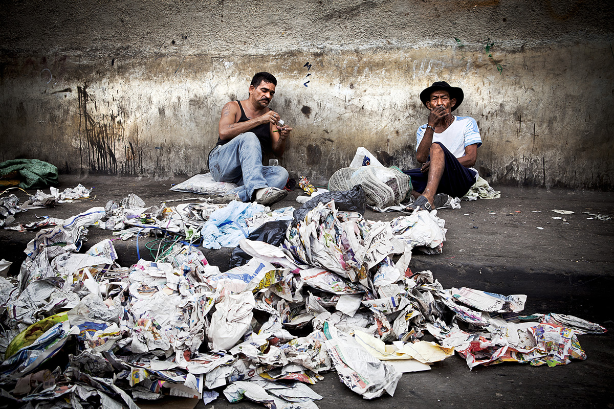 Man on the left refills crack pipe while man on right smokes a cigerette as they wait for recyclables to arrive. Barranquilla, Colombia 2014.