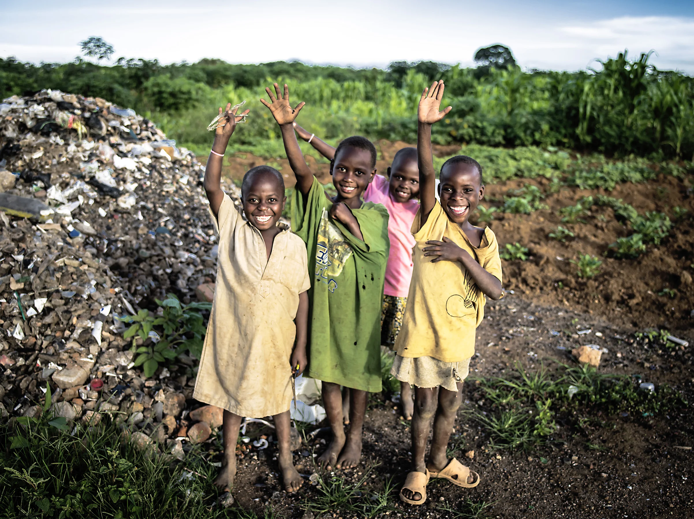 Local children wave hello from a dumpsite where they are looking for materials to sell. Mbarara.