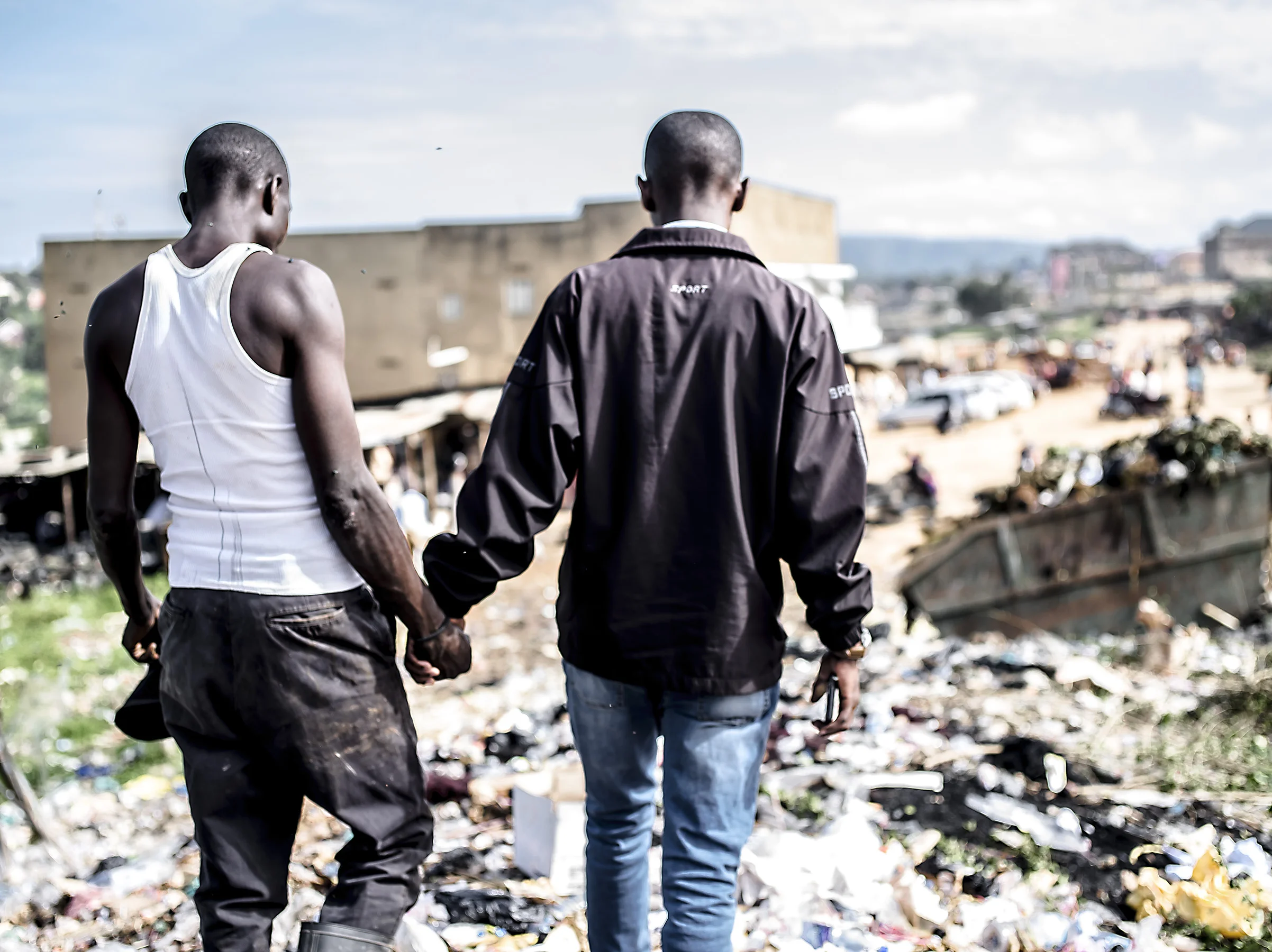 Taremwa Sam Rwabwehare holds hands with an informal recycler as they lead one another through the trash to talk about the worker's life, his work and the area. Mbarara.