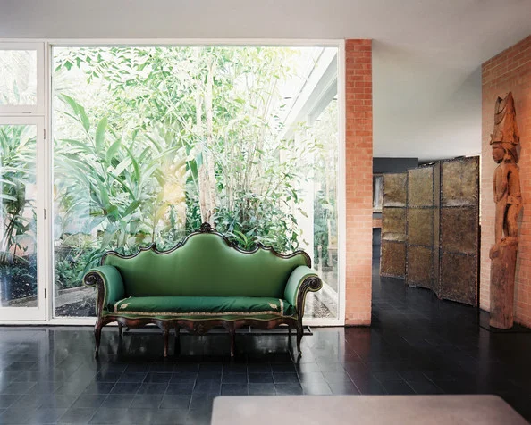 A green sofa in front of a wall of windows (Source: Lonny) 