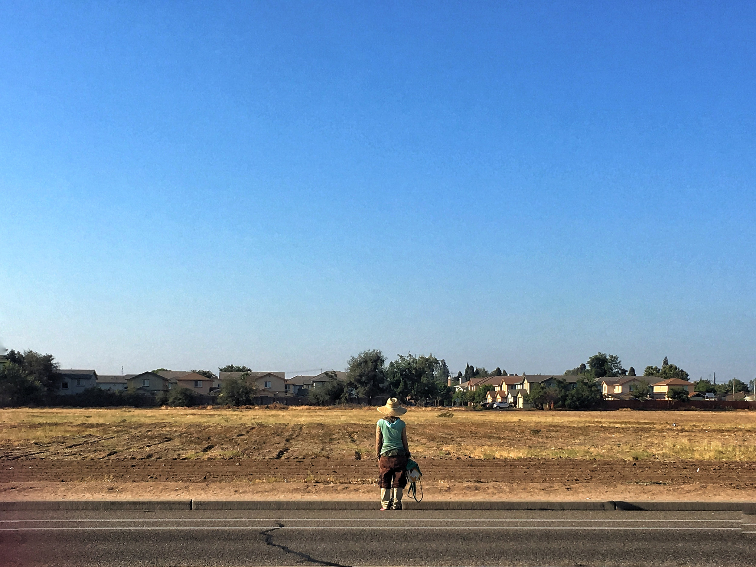 a woman stops to ponder the horizon at a empty plot of land nestled in a subdivision