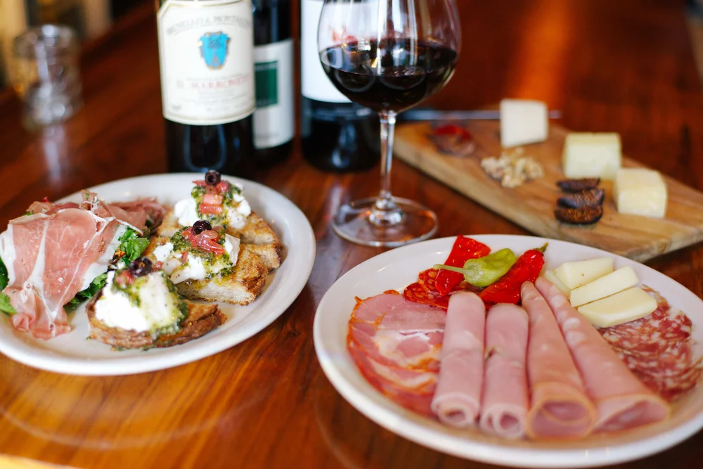 Plate of proscutto alongside a plate of bruschetta with a glass of red wine