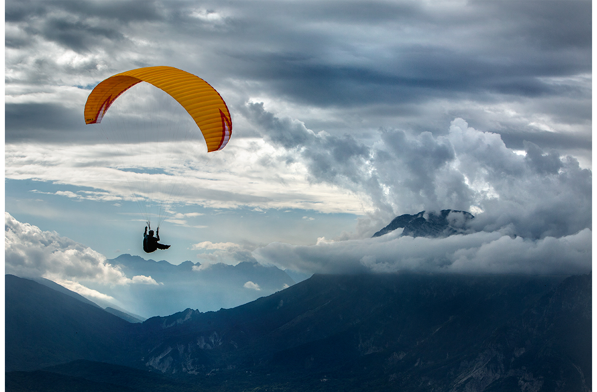 Paraglider riding the thermals on the ridge above Meduno, Italy.