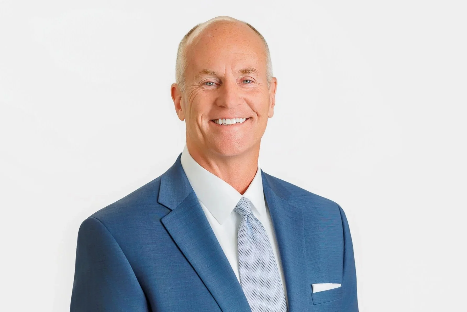 Headshot of man in a blue suite with light blue tie against a white backdrop