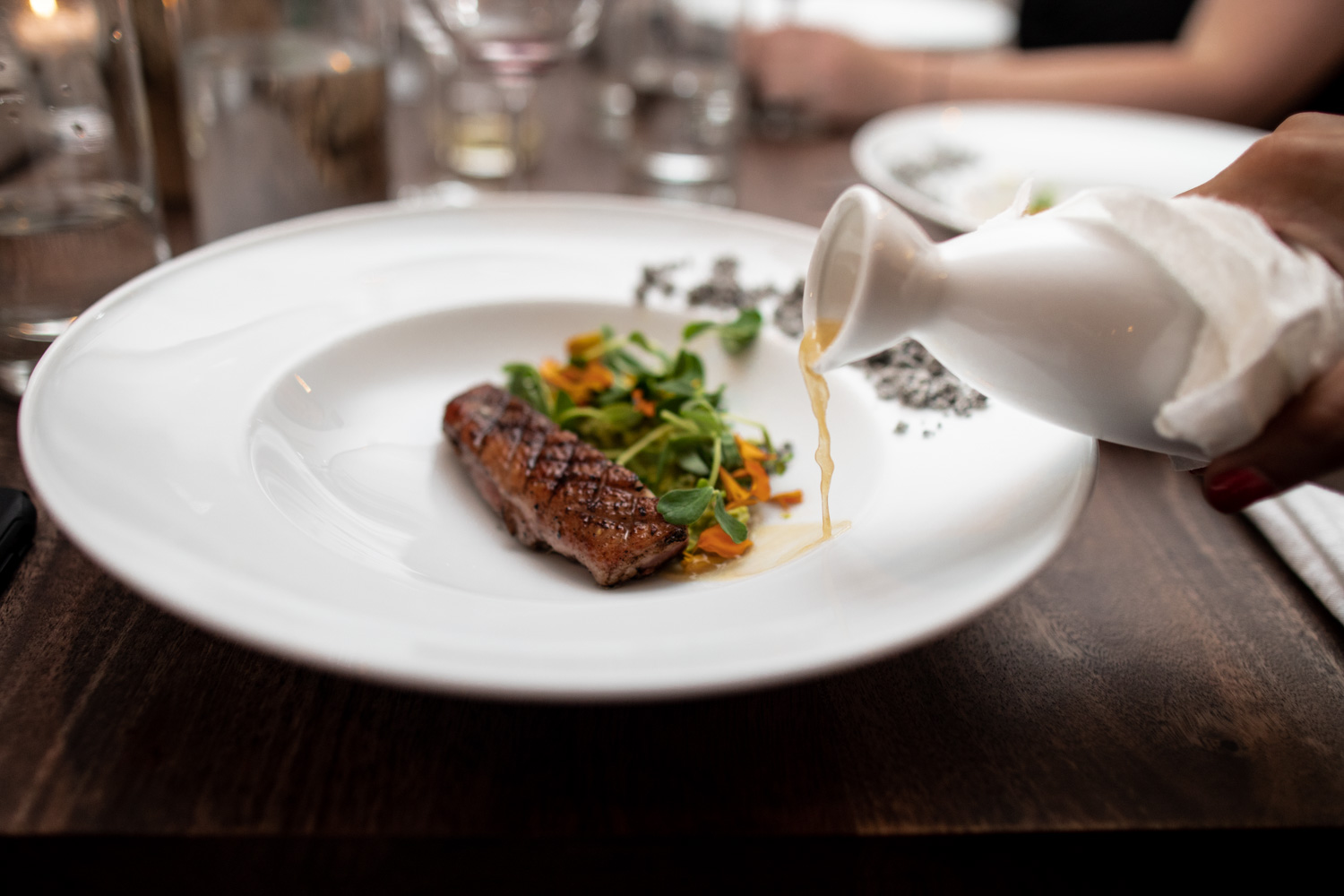 Serving of the duck (72 hour prep) with caramelized onion broth, field pea & mint pistou, earl grey ash, and pea shoots.