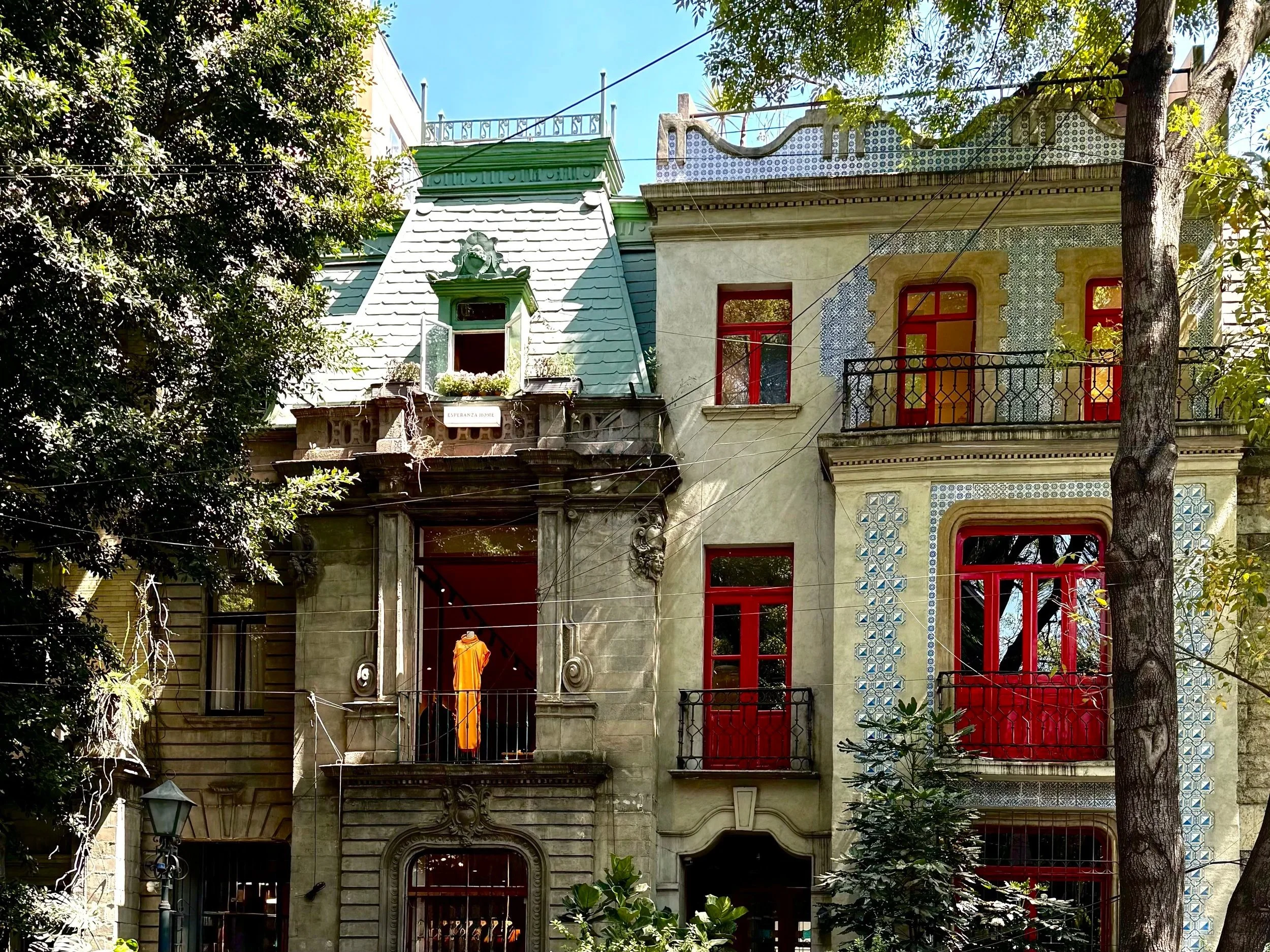 Buildings in Mexico City showing different architectural styles, tiles, red window casings, orange dress on a balcony in a shop.
