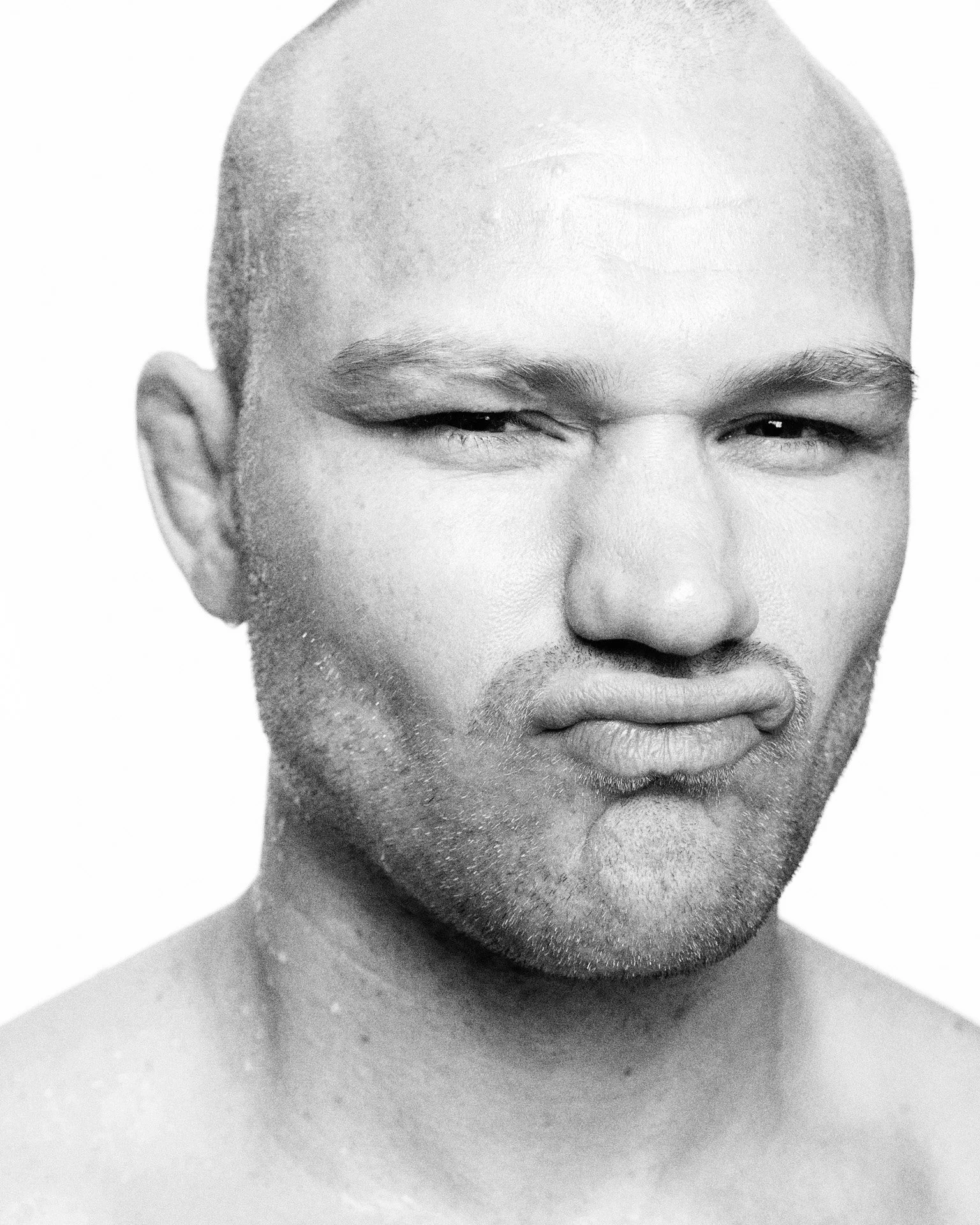 Sort/hvidt foto af en mand med kort hår, der smiler med det ene øje halv-tilt, mens han har et skæg.