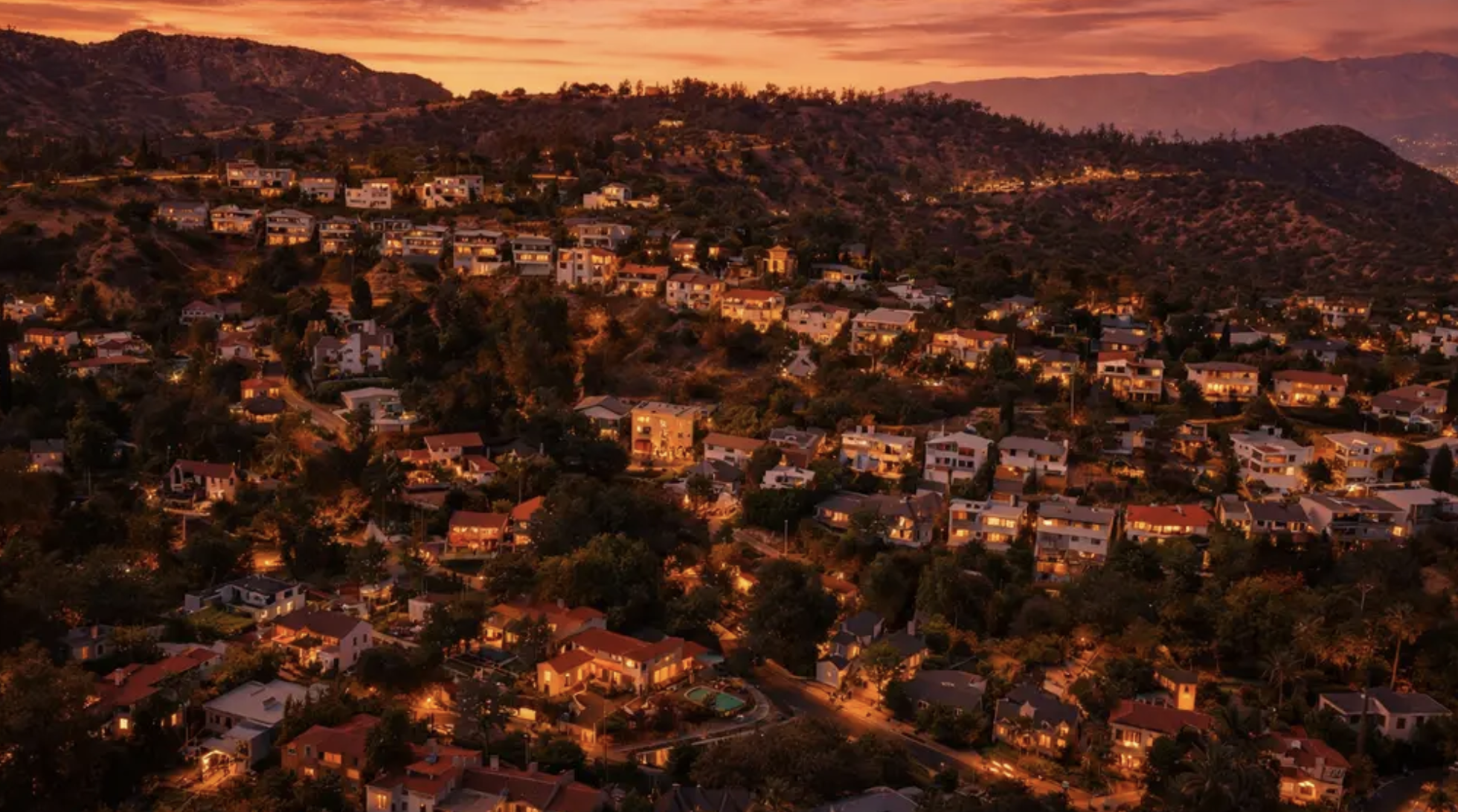 Homes lit up across the hillside of the Los Feliz Oaks at sunset, with the Griffith Park hills behind them.
