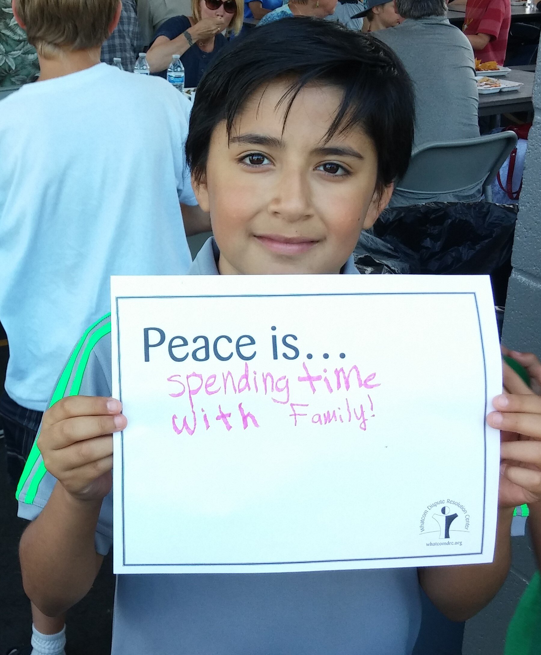 一个小男孩举着 WDRC 标志，上面写着 "和平就是......与家人共度时光！"