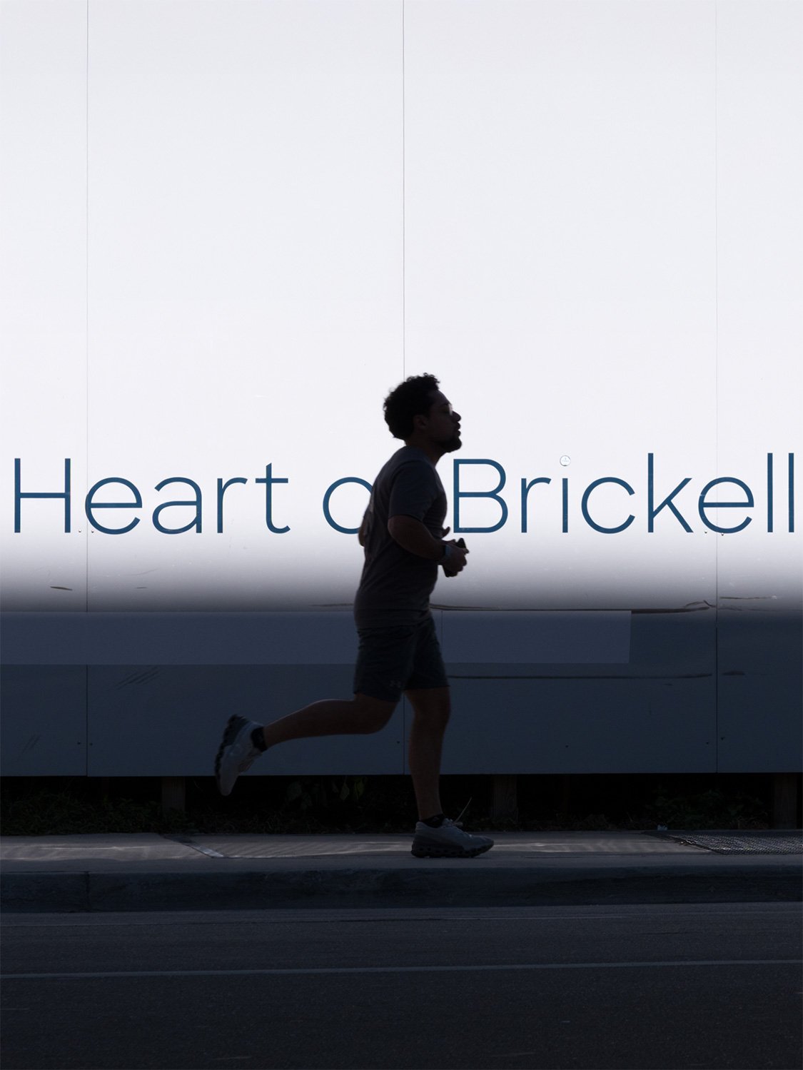 Runner jogging in Brickell Miami urban neighborhood near luxury real estate development signage.