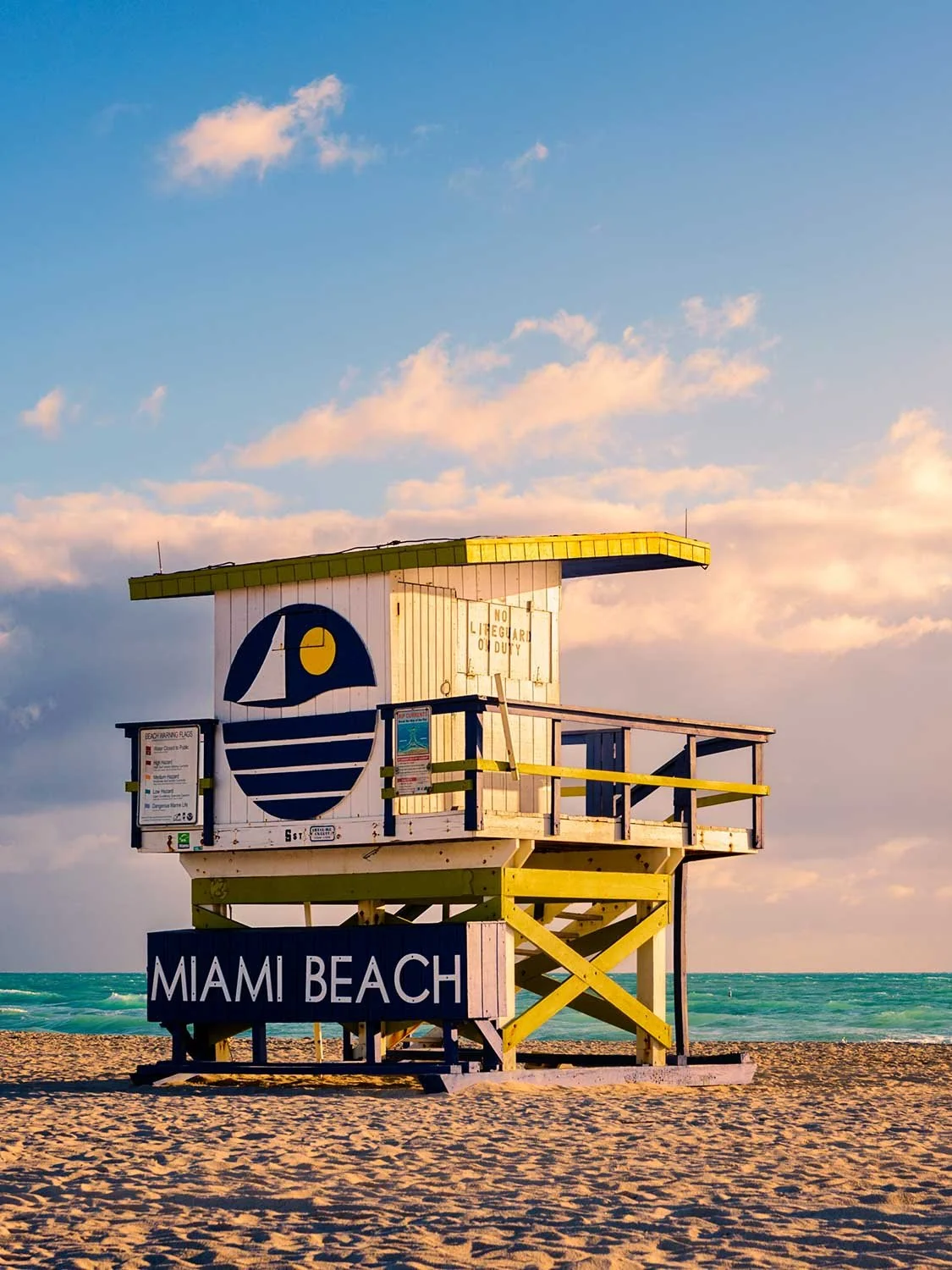 Miami Beach lifeguard stand on sandy shore with turquoise ocean waves and pastel blue sky at golden hour