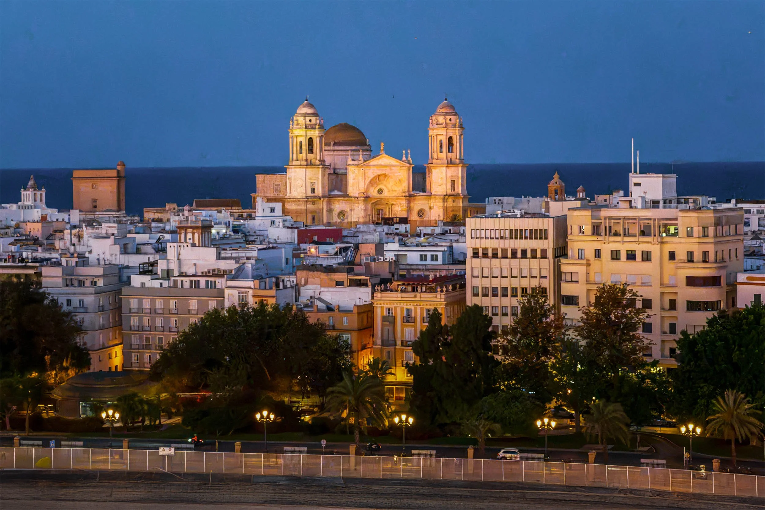 Cadiz Cathedral illuminated at dusk with city rooftops and Atlantic Ocean in background, Spain