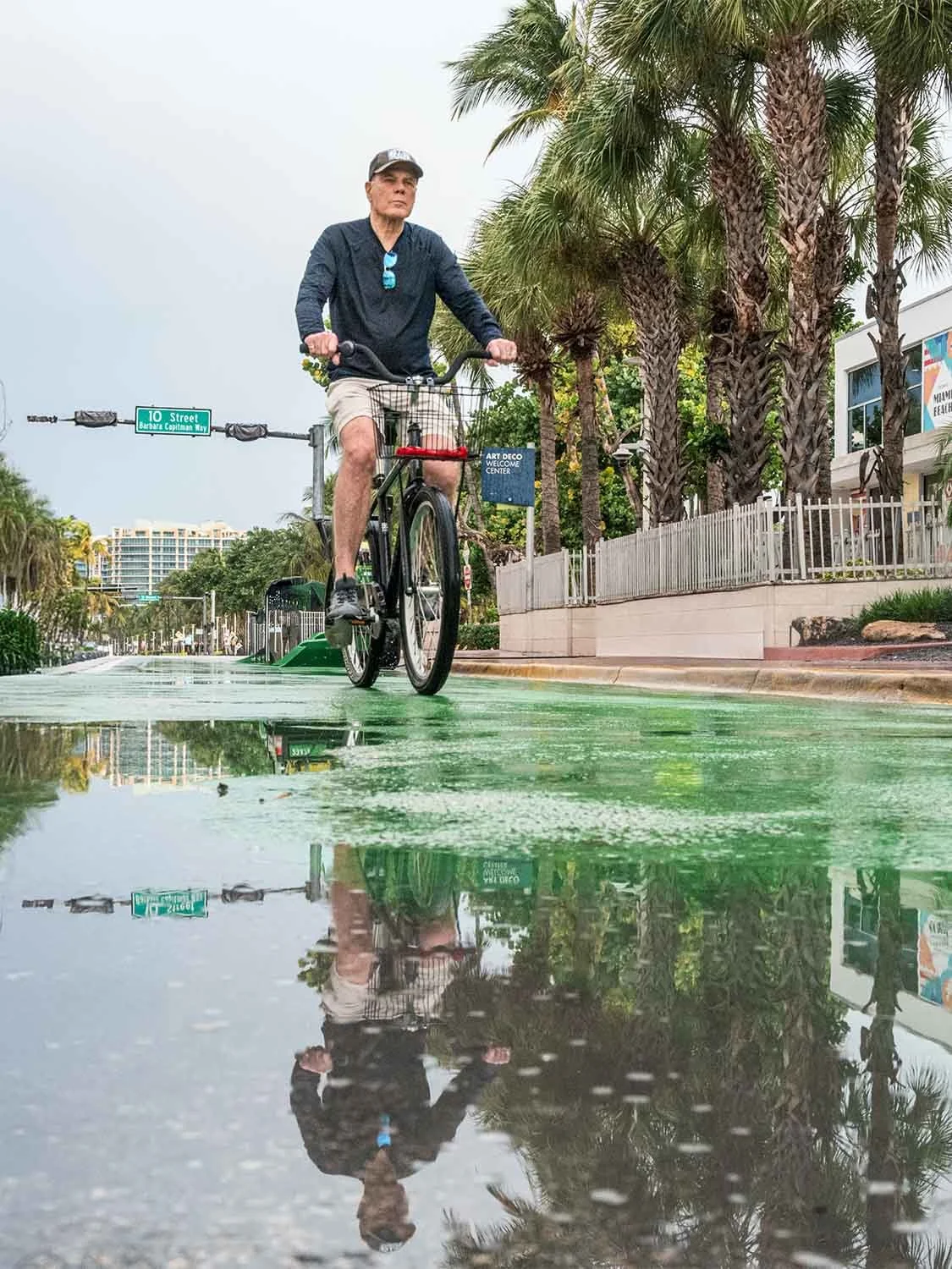Man riding a bicycle on a wet green bike lane near the Art Deco Welcome Center on 10th Street in Miami Beach
