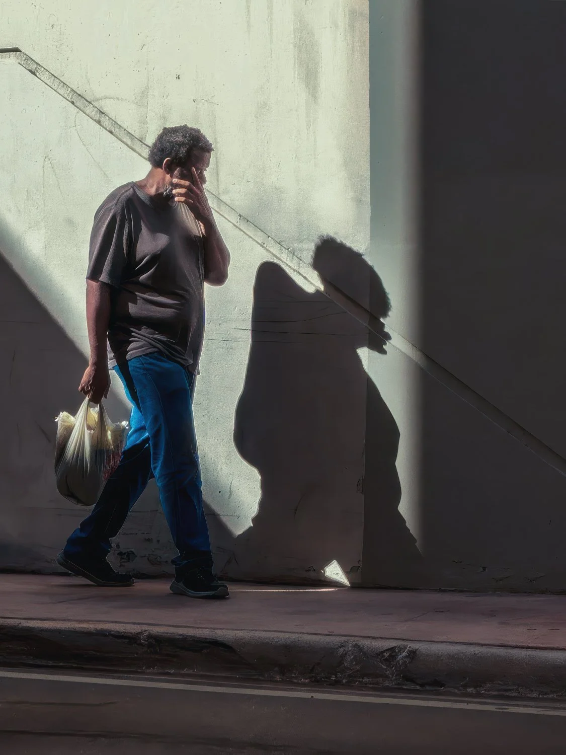Man walking through a shaft of sunlight against a white wall in Miami, dramatic shadow cast beside him at midday