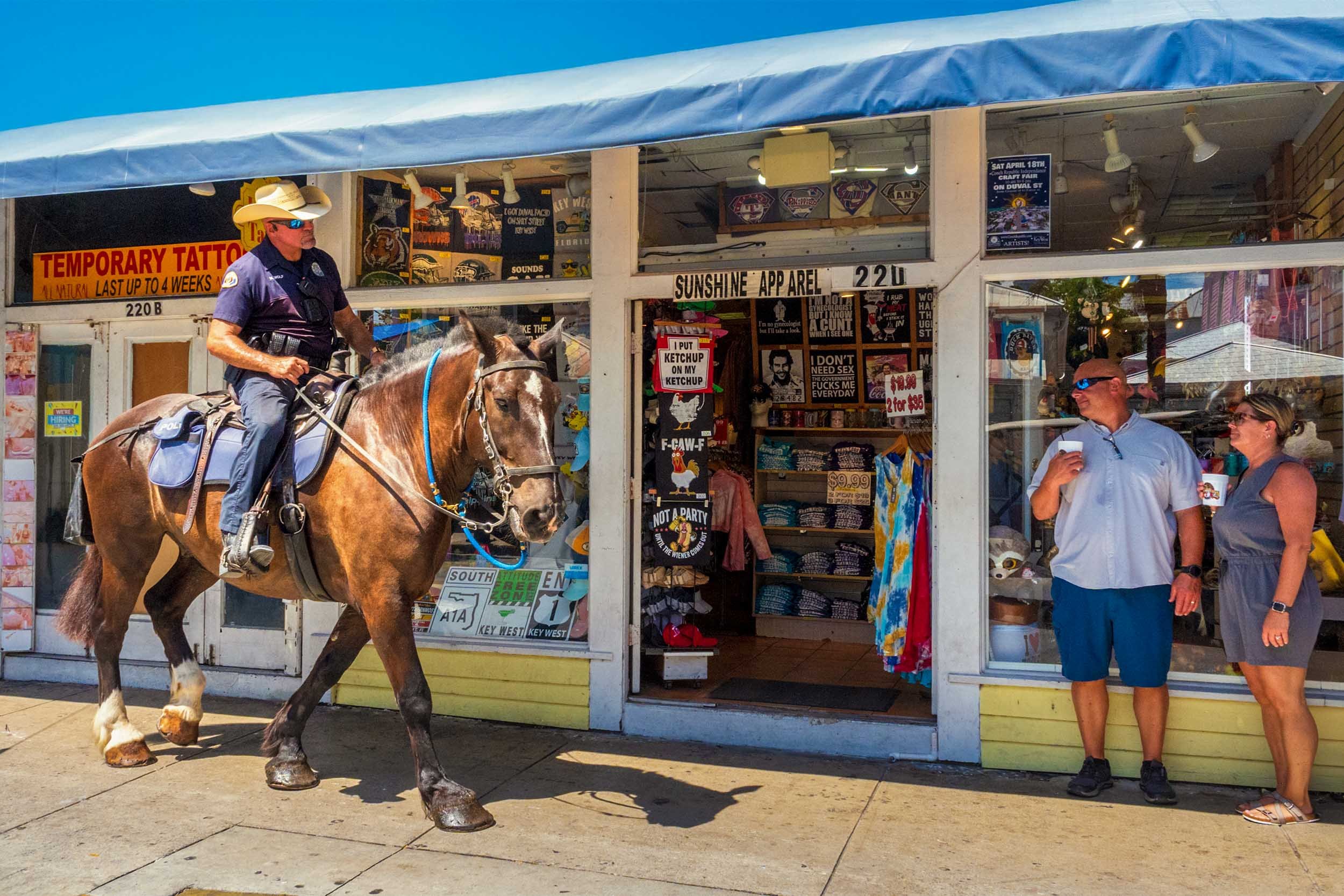 Mounted police officer on horseback patrolling Duval Street in Key West past a souvenir shop with tourists nearby
