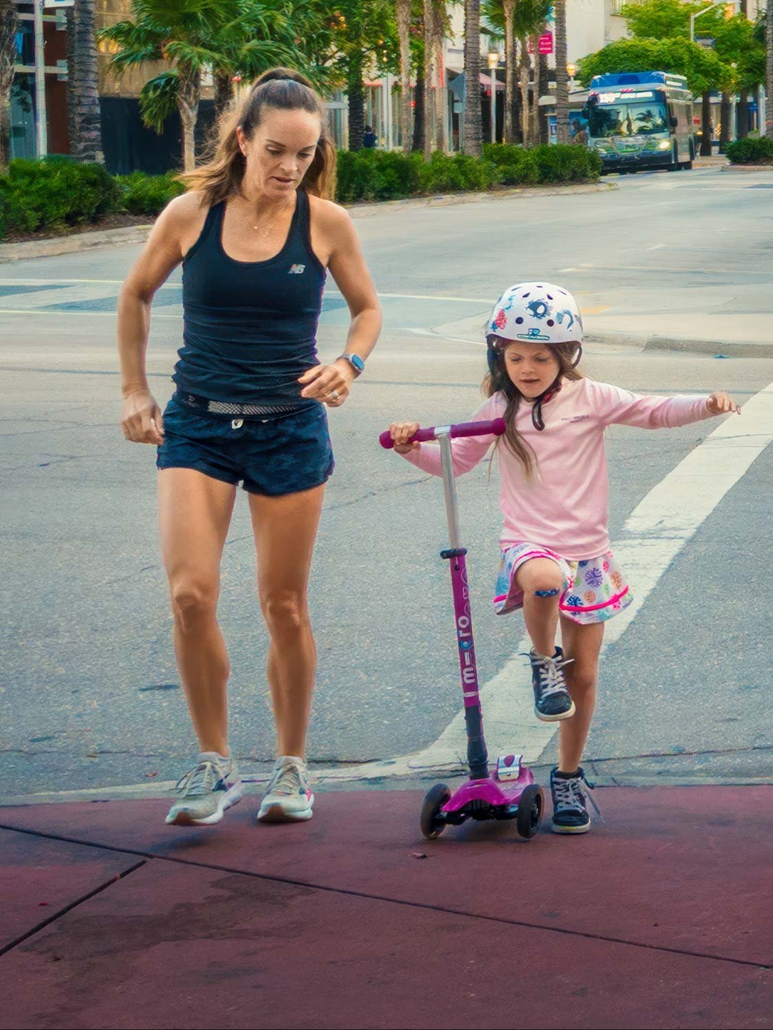 Child riding scooter with adult jogging beside her on Miami street capturing movement lifestyle and everyday life