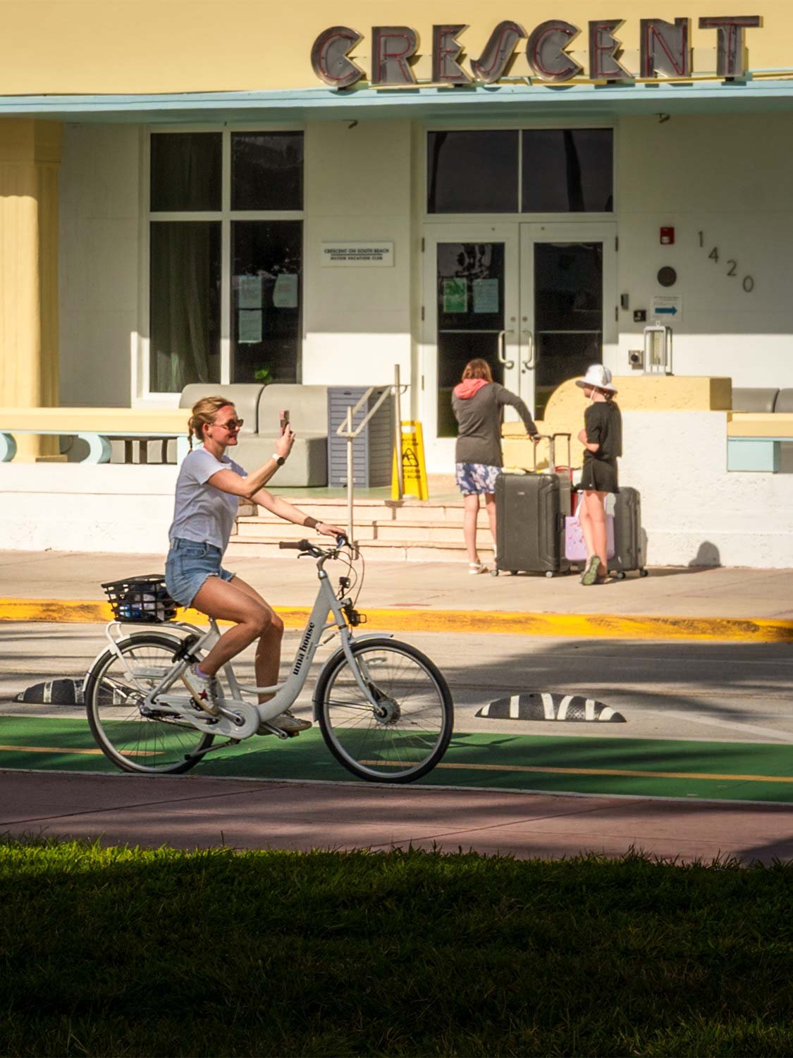 Woman riding a white cruiser bike on a green bike lane in front of the Crescent hotel on South Beach