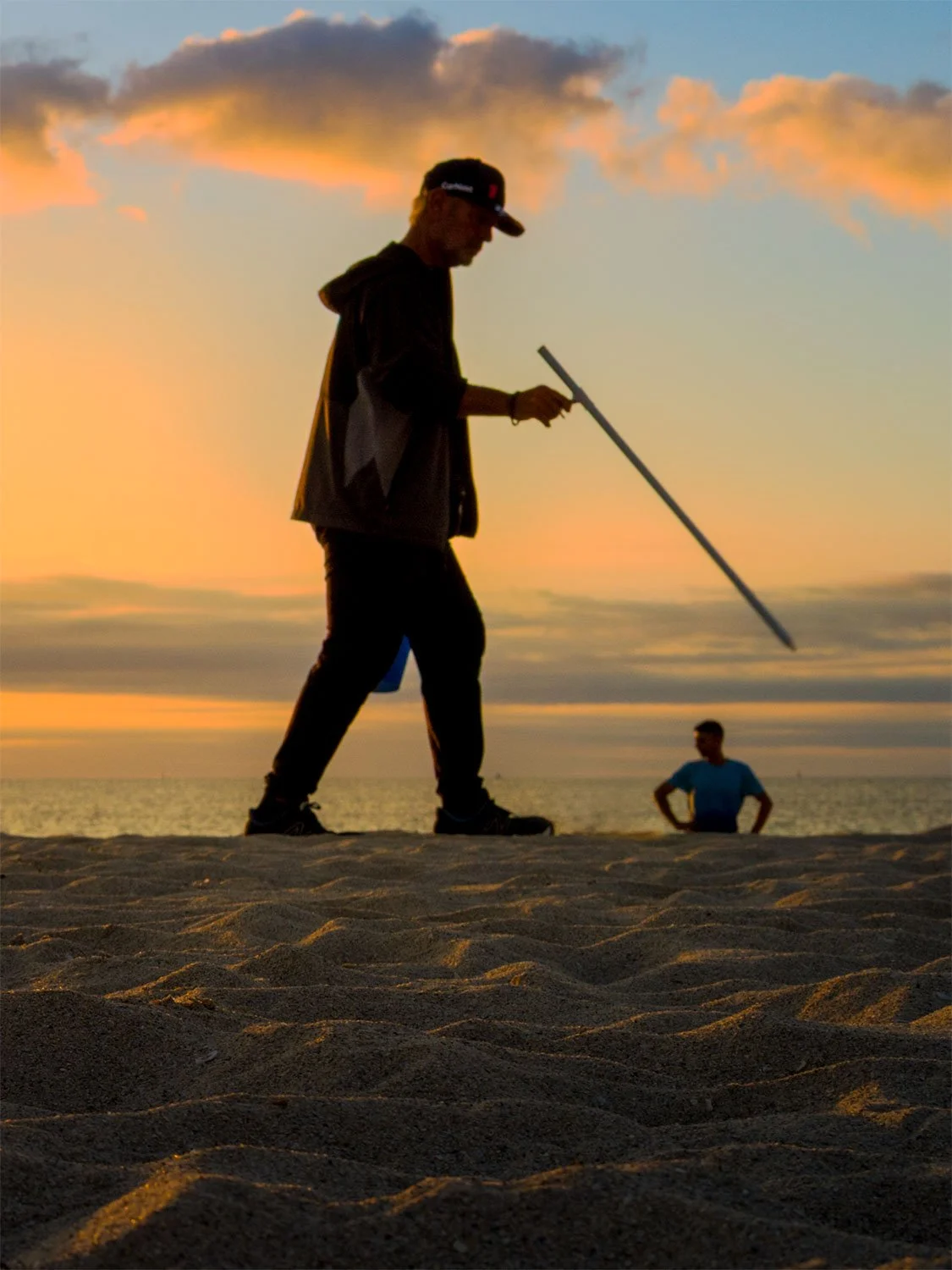 Beach worker carrying a squeegee silhouetted against a golden sunrise on South Beach Miami