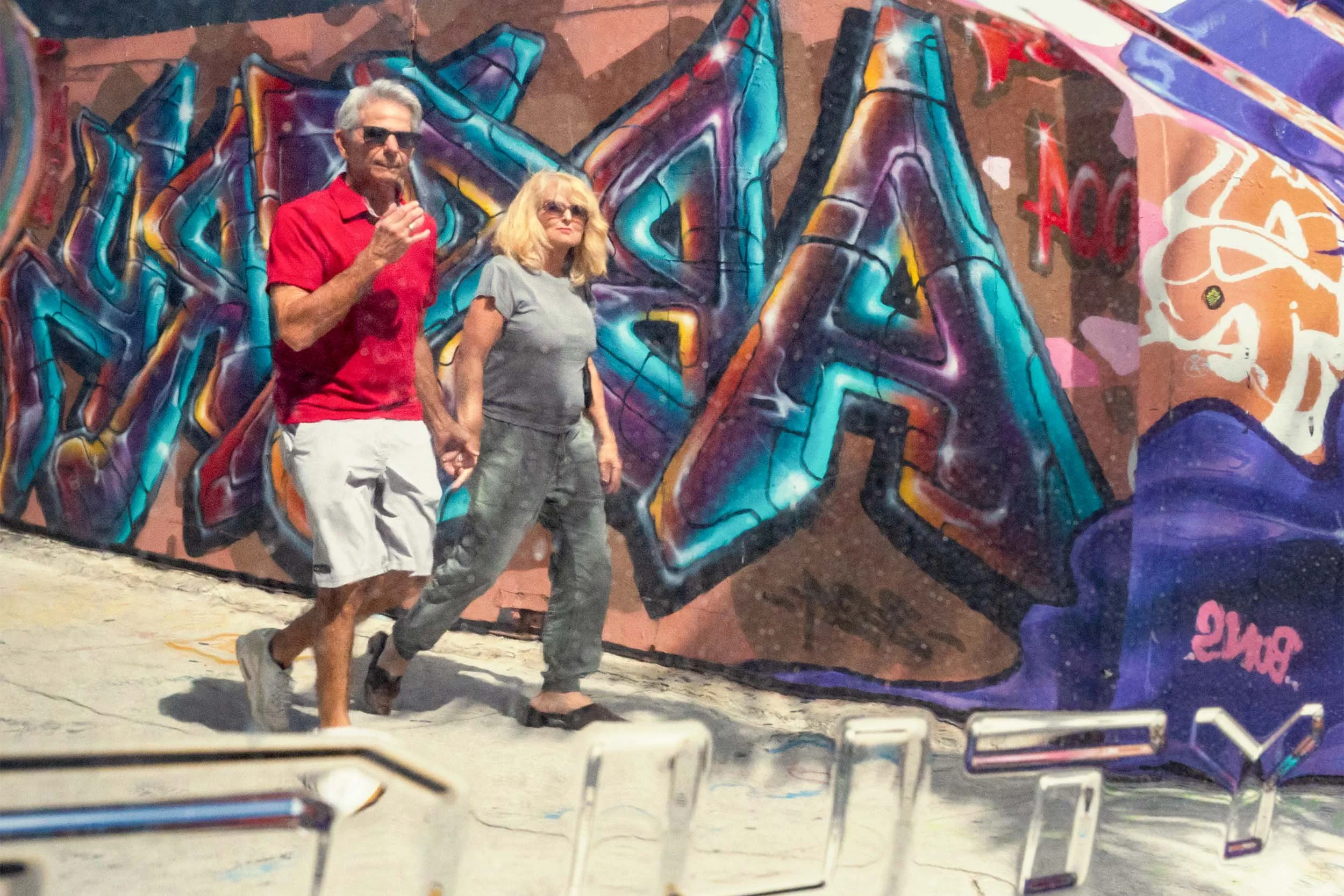 Couple walking hand in hand past a large colorful graffiti mural in Wynwood Miami