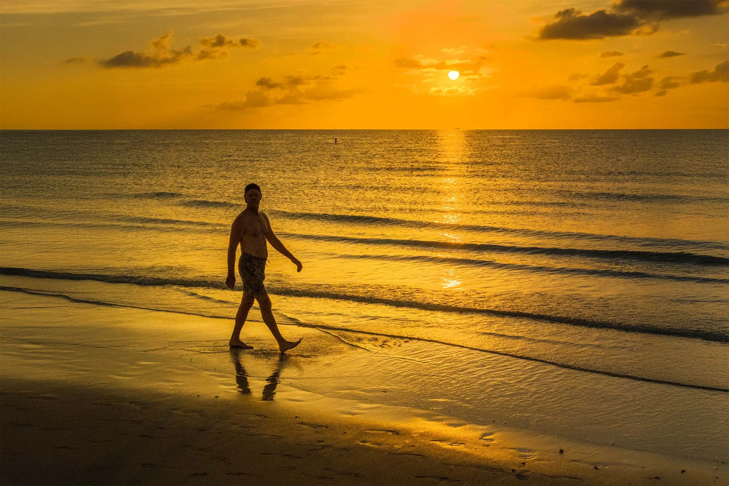 A silhouette walks alone at the edge of the water at sunrise on South Beach in Miami Beach