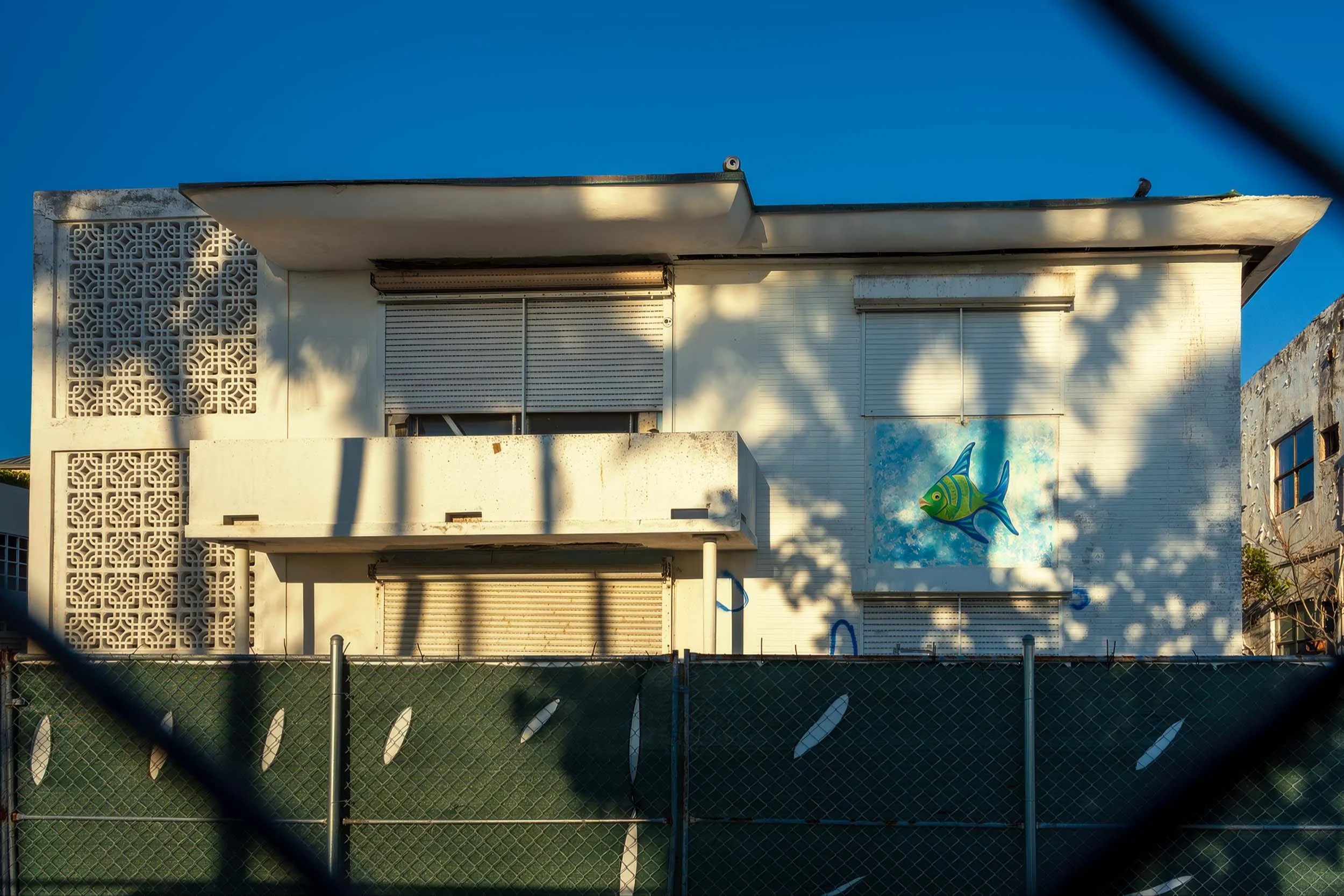 Wide view of 7400 Ocean Terrace hotel with roll-down shutters and painted fish mural