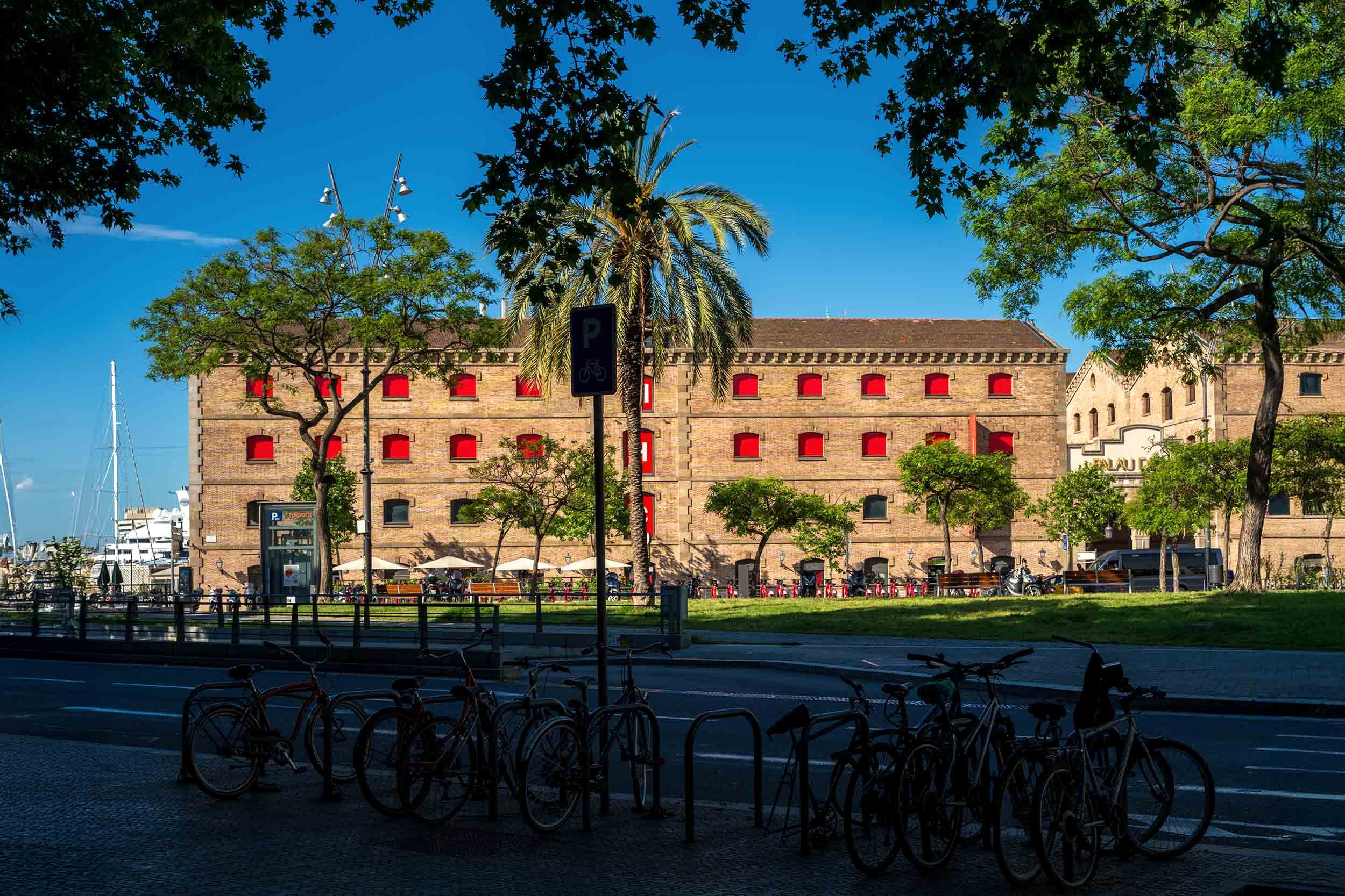 The brick Palau de Mar warehouse with red window shutters along the Port Vell waterfront, bicycles parked in the foreground