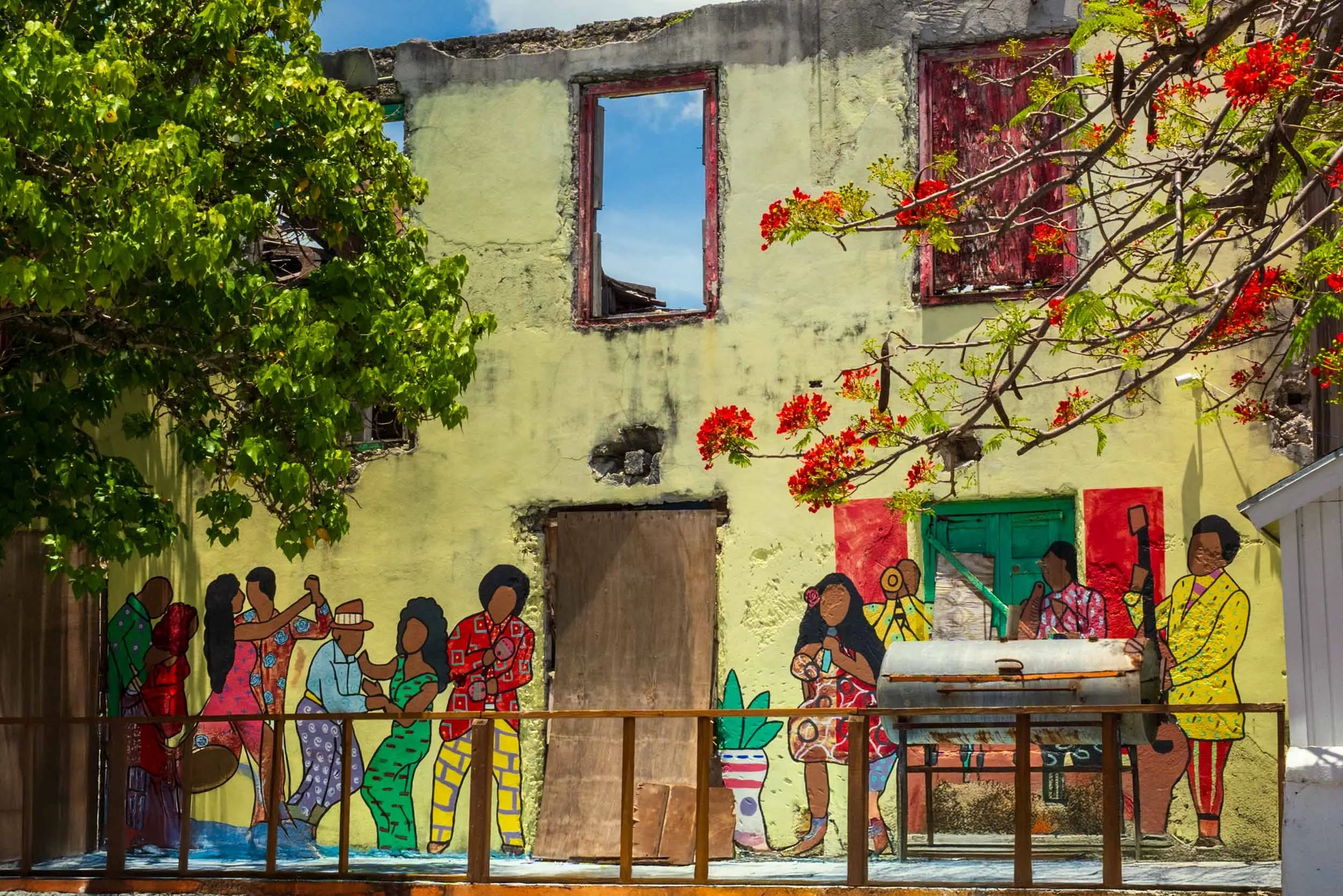 Caribbean street art mural colorful figures urban decay yellow wall flamboyant tree tropical culture