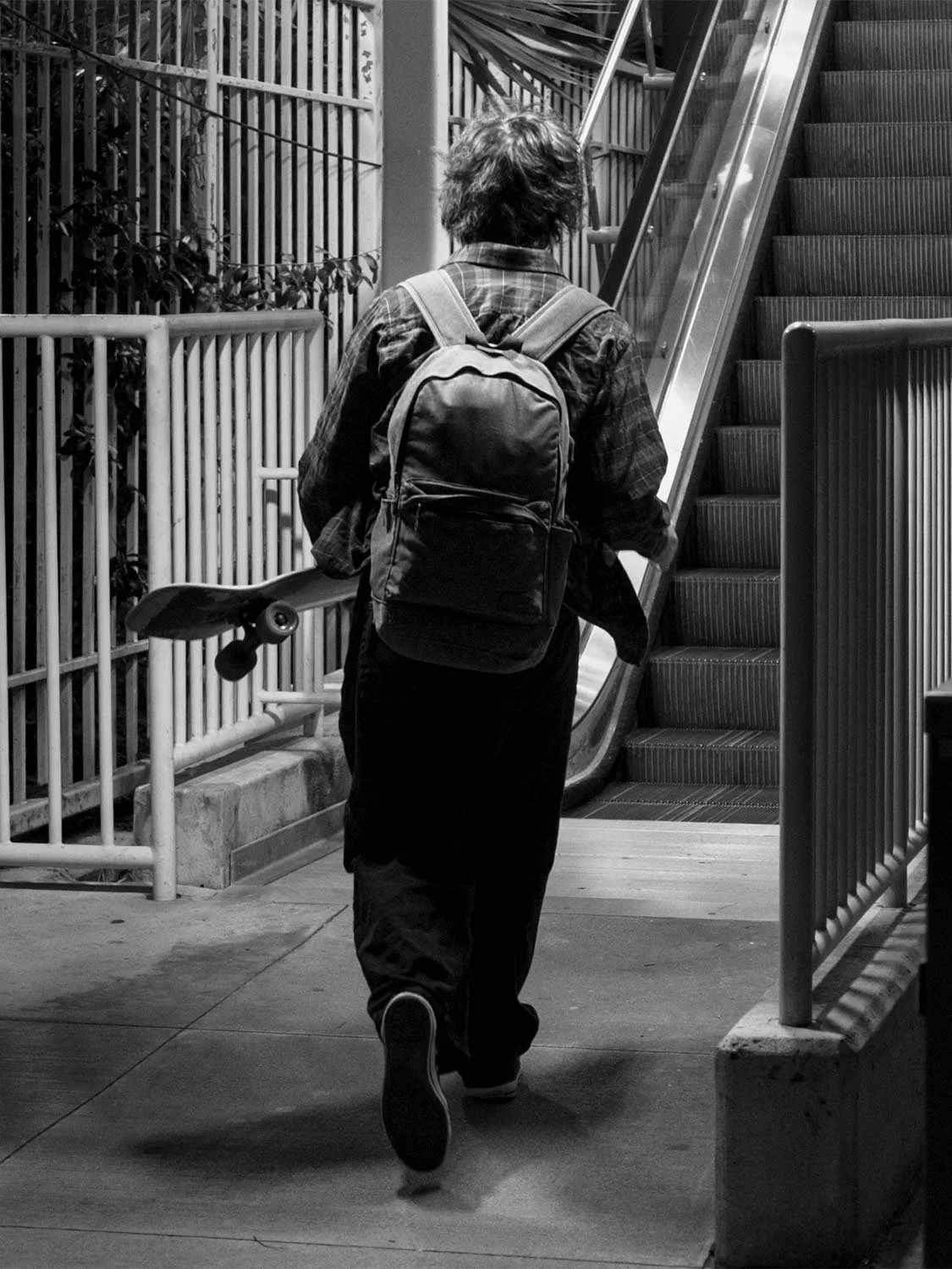 Skateboarder walking through Brickell, Miami with longboard and backpack, black and white street photography