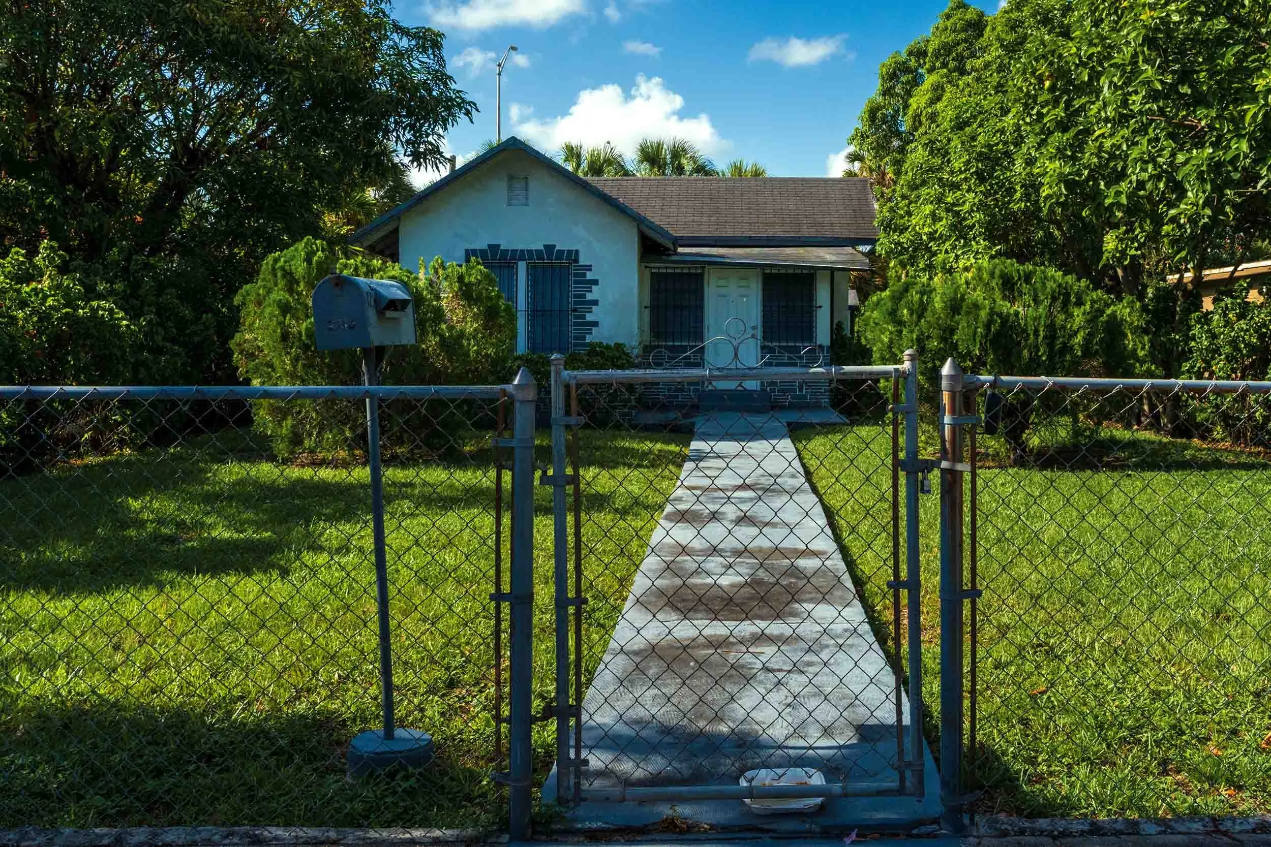 Blue and white bungalow behind a chain-link gate and mailbox, Buena Vista Miami
