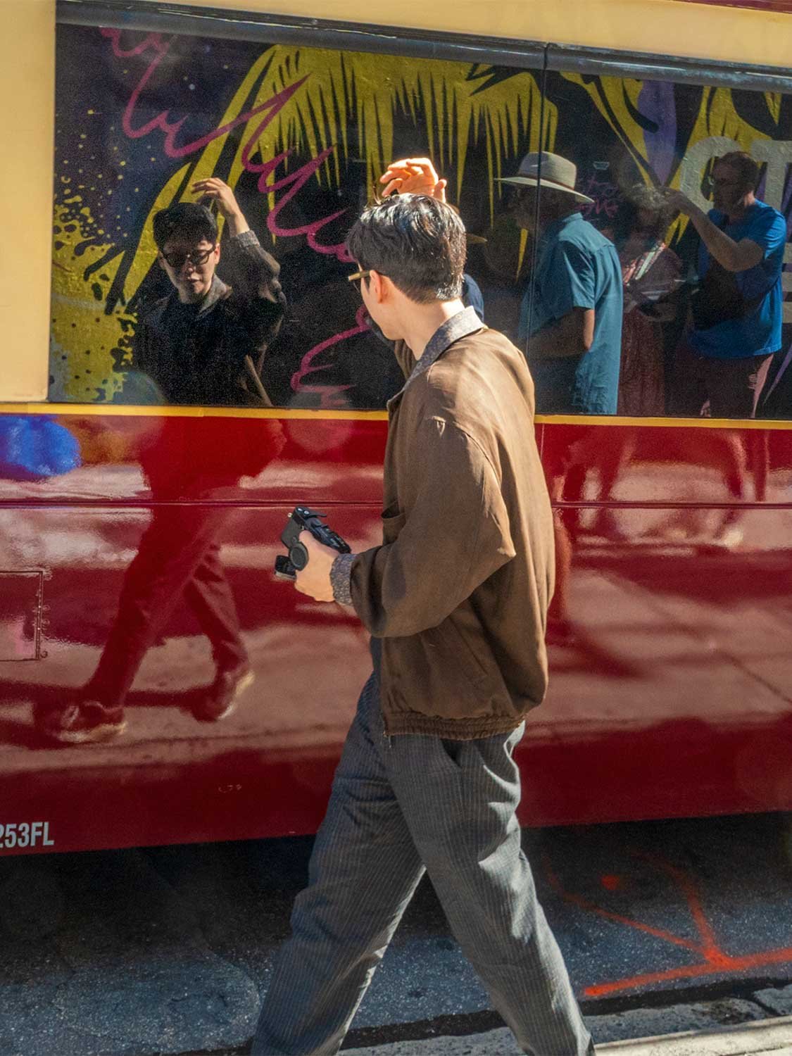 Photographer walking past a painted Miami trolley bus reflecting the street scene in its glossy red side panels