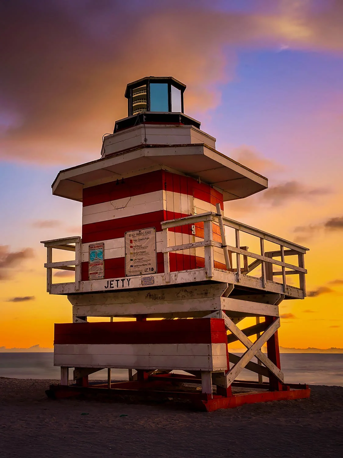 Red and white striped Jetty lifeguard tower on Miami Beach at golden sunset with dramatic purple sky