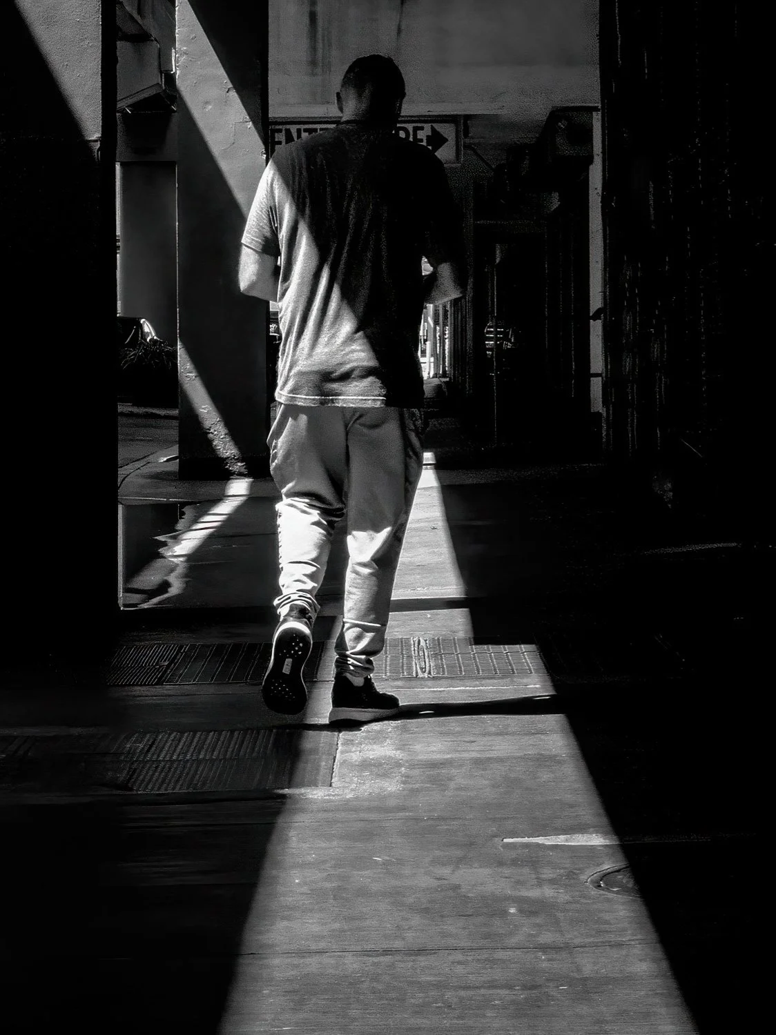 Man walking away from camera through a corridor of light and shadow in black and white, Miami